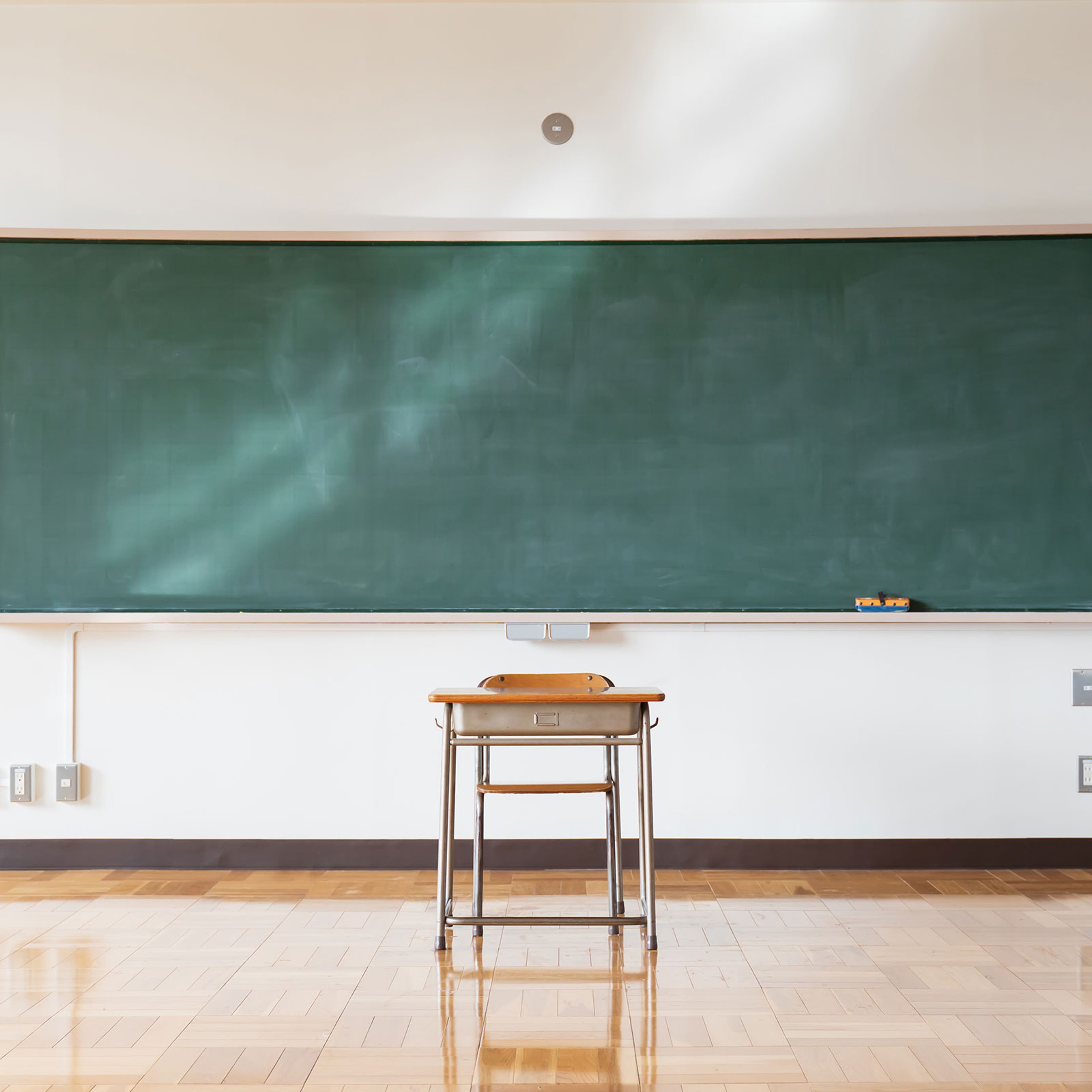 A single desk sitting in front of a blackboard in a classroom
