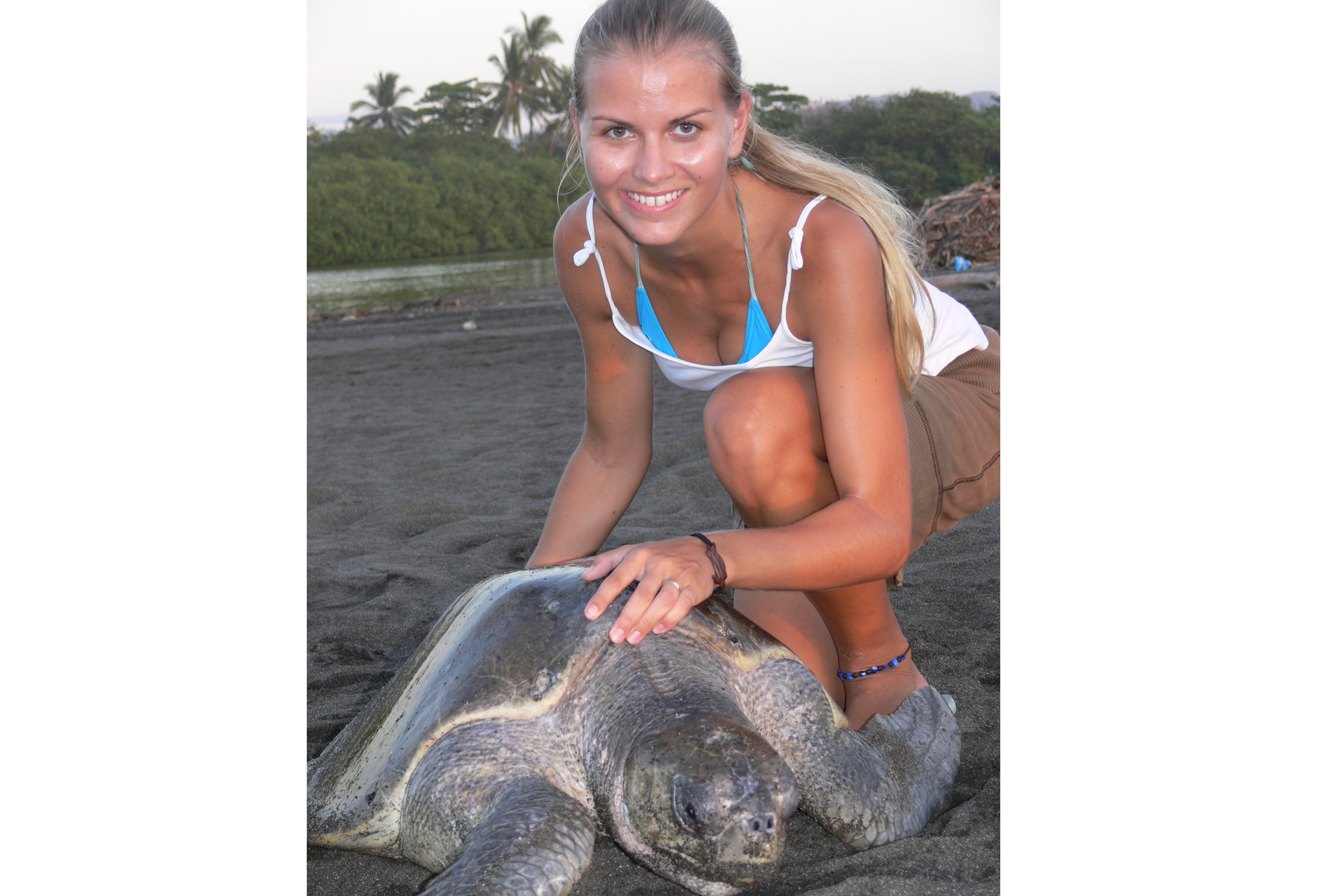 Christine Figgener smiles at the camera with a sea turtle on the sand