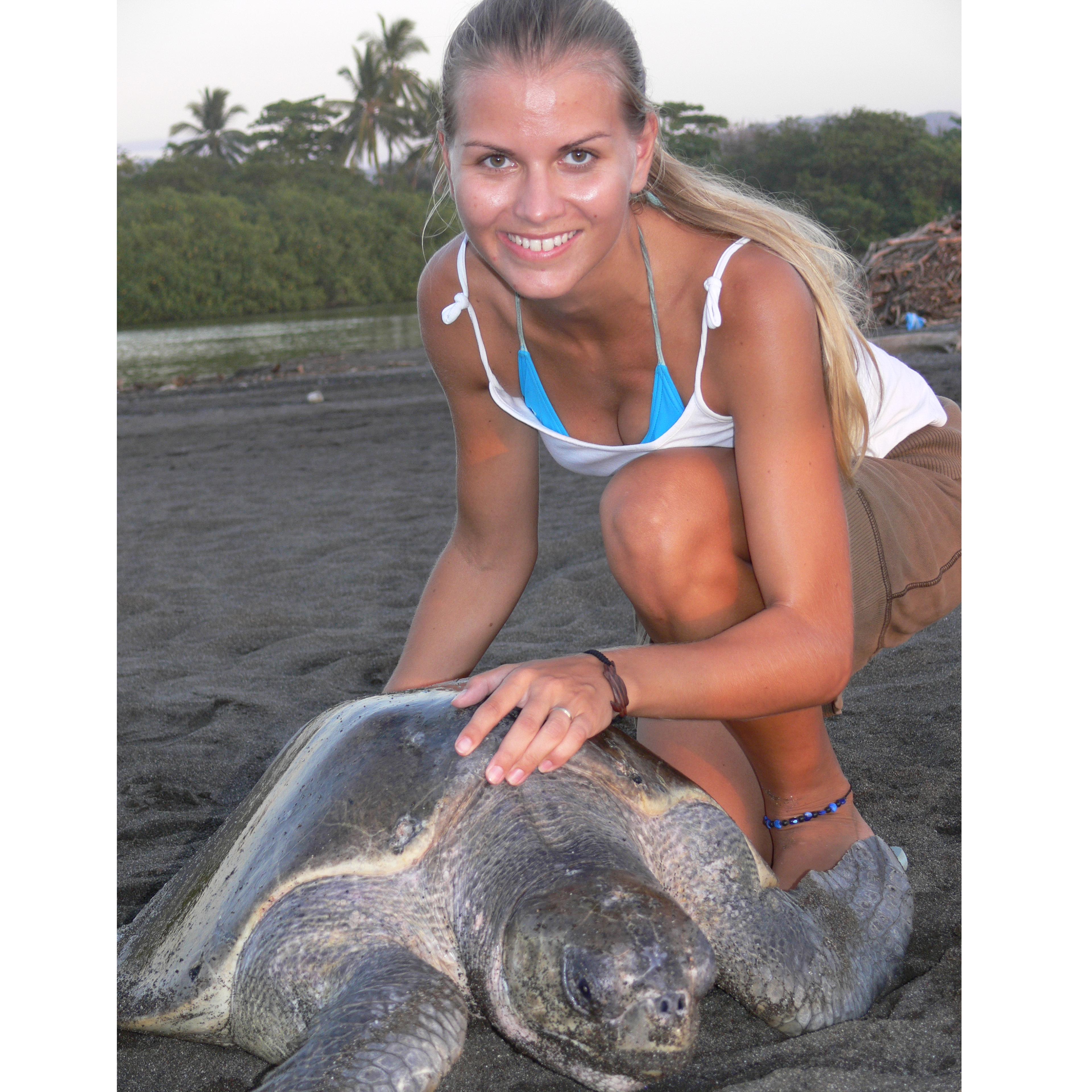 Christine Figgener smiles at the camera with a sea turtle on the sand
