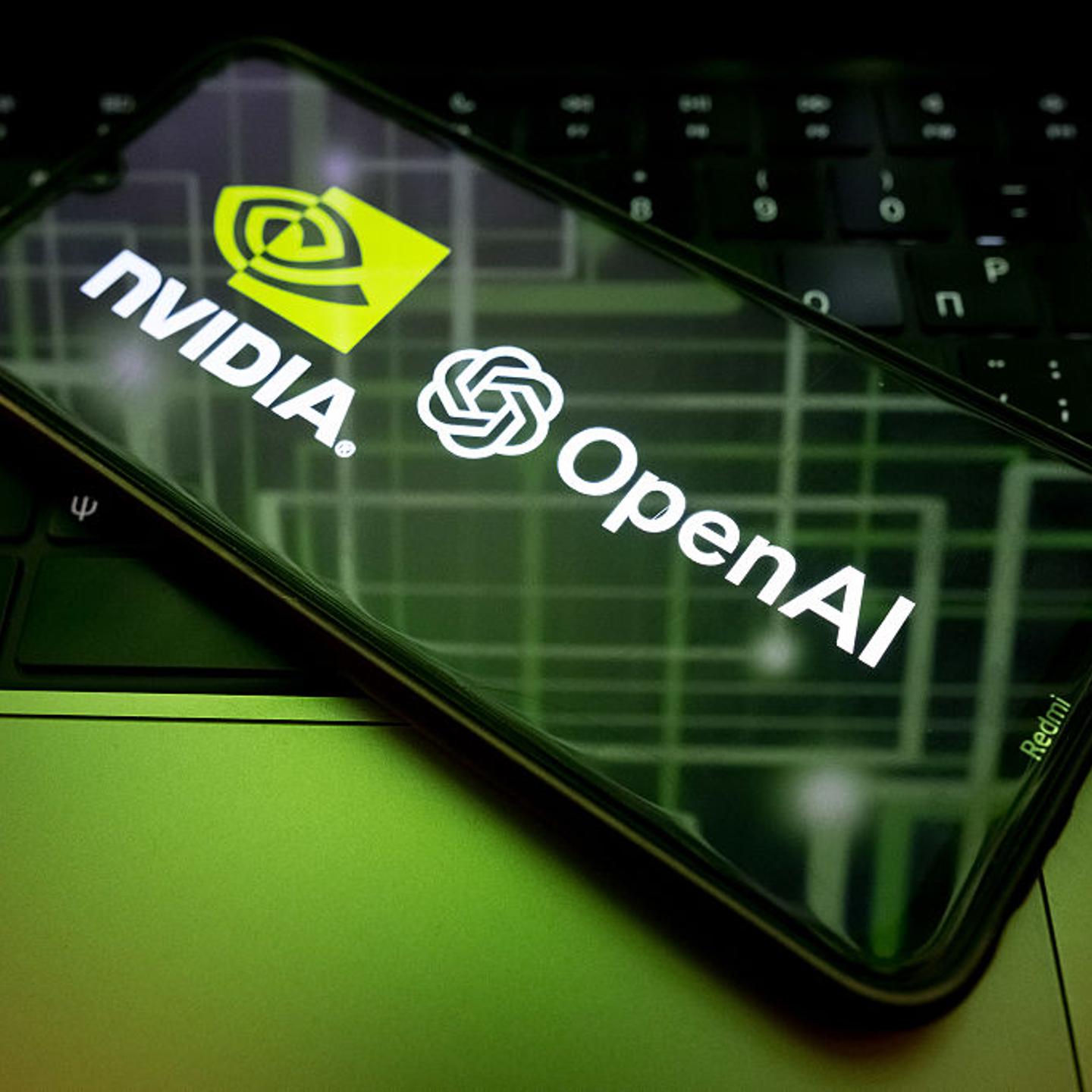 The Nvidia and OpenAI logos are seen on a phone screen in front of a laptop with green lighting.