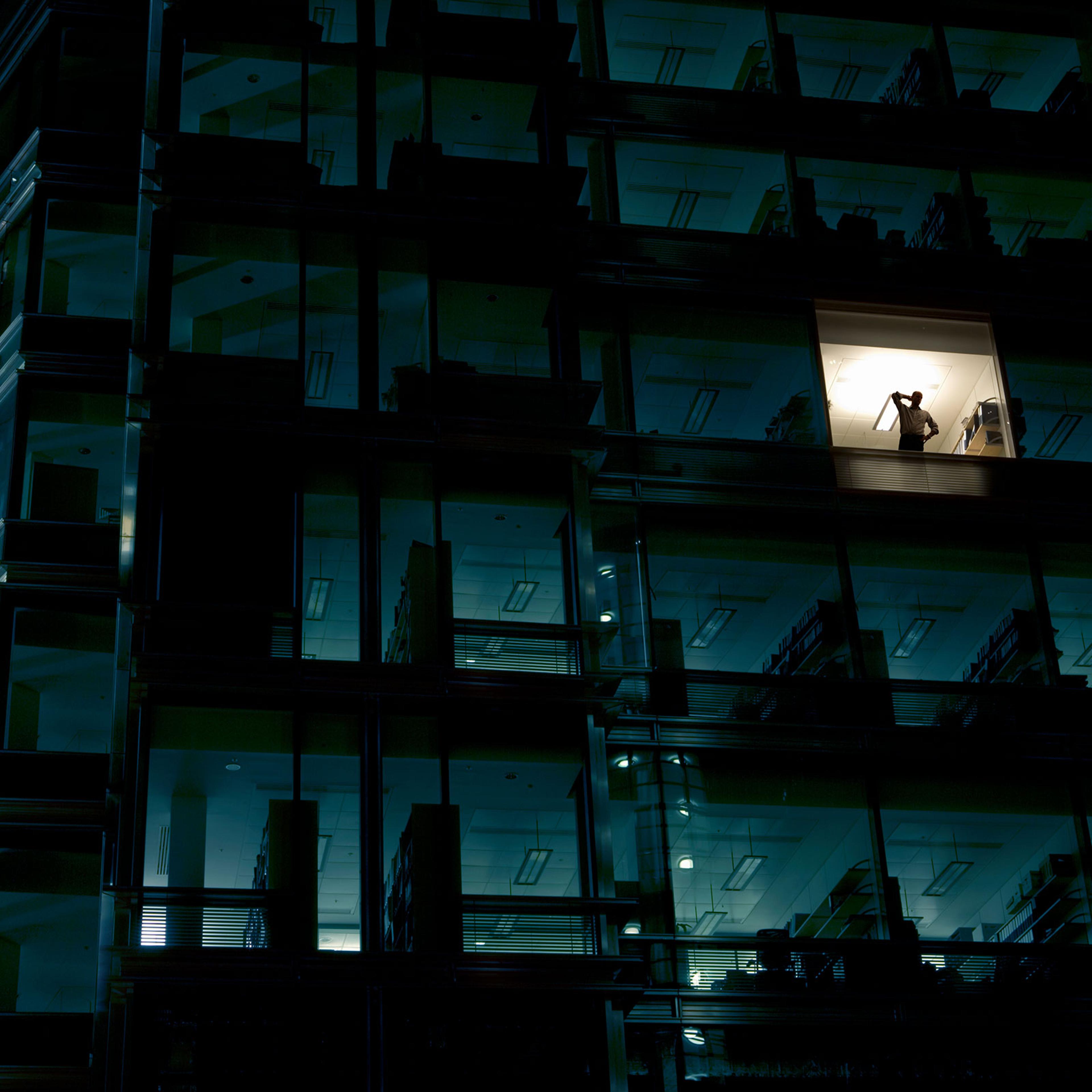 Office building at night, man standing in one illuminated window, low angle view