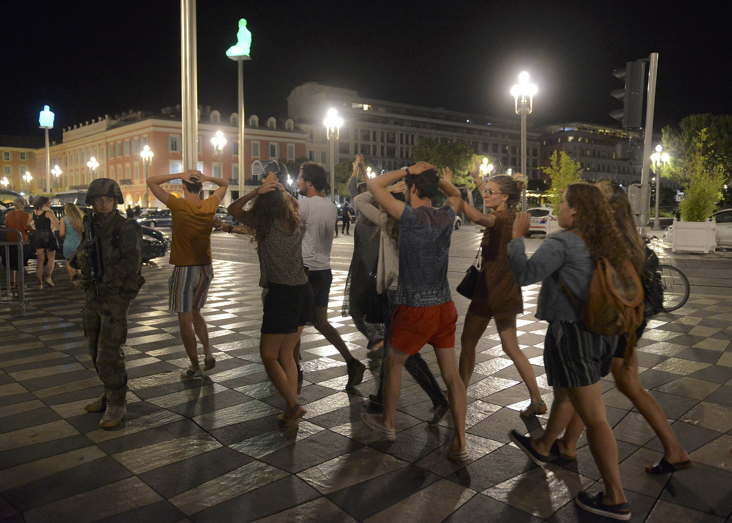 People cross the street with their hands on their heads as a French soldier secures the area in Nice, France, on July 15, 2016, after at least 60 people were killed along the Promenade des Anglais when a truck ran into a crowd celebrating Bastille Day.