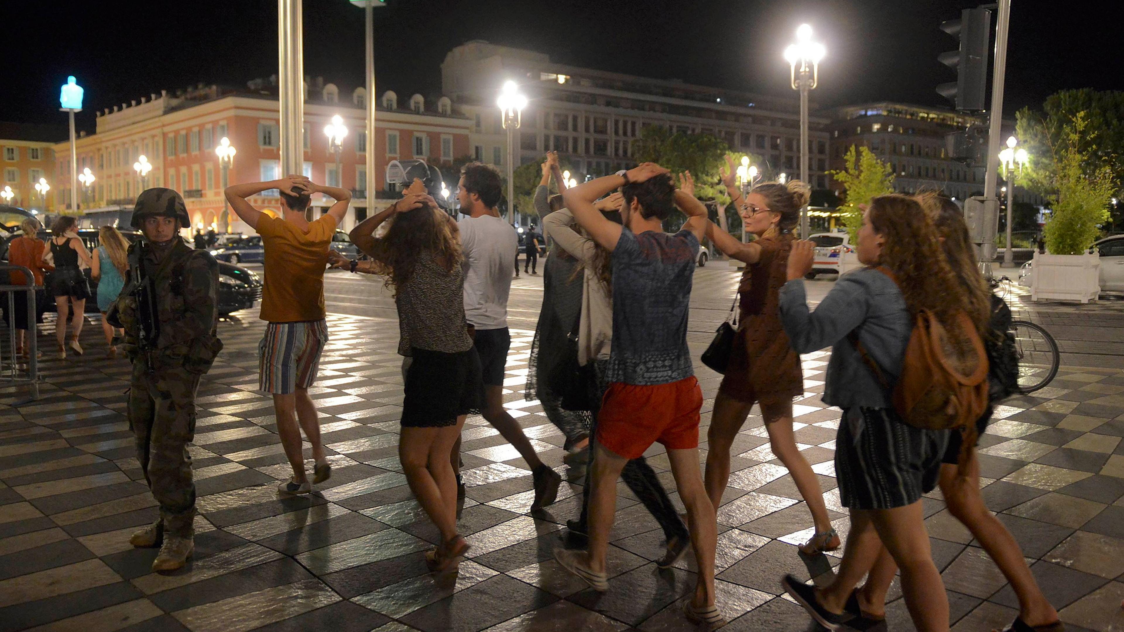 People cross the street with their hands on their heads as a French soldier secures the area in Nice, France, on July 15, 2016, after at least 60 people were killed along the Promenade des Anglais when a truck ran into a crowd celebrating Bastille Day.