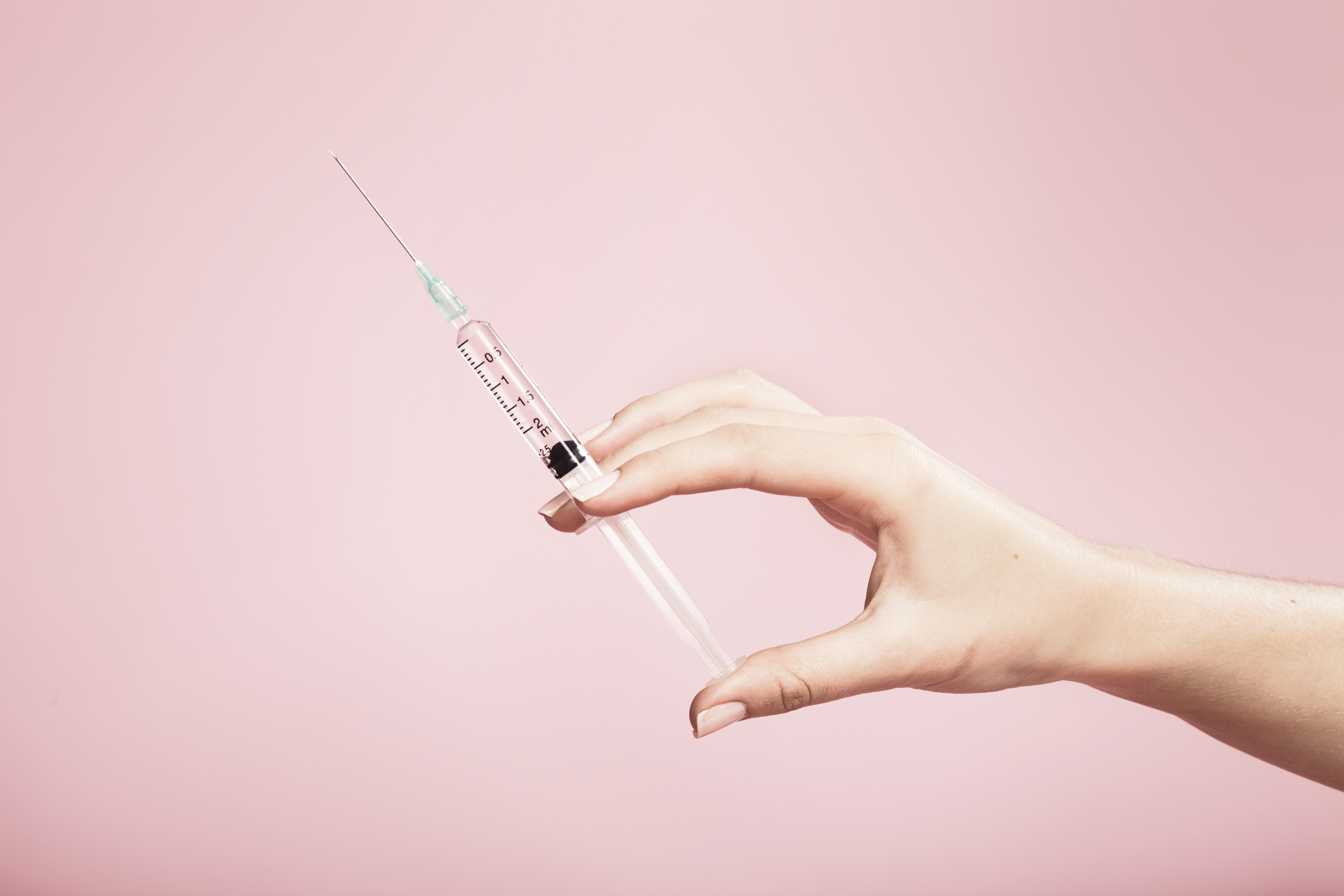 Hand holding syringe in plain pink background TIME health stock