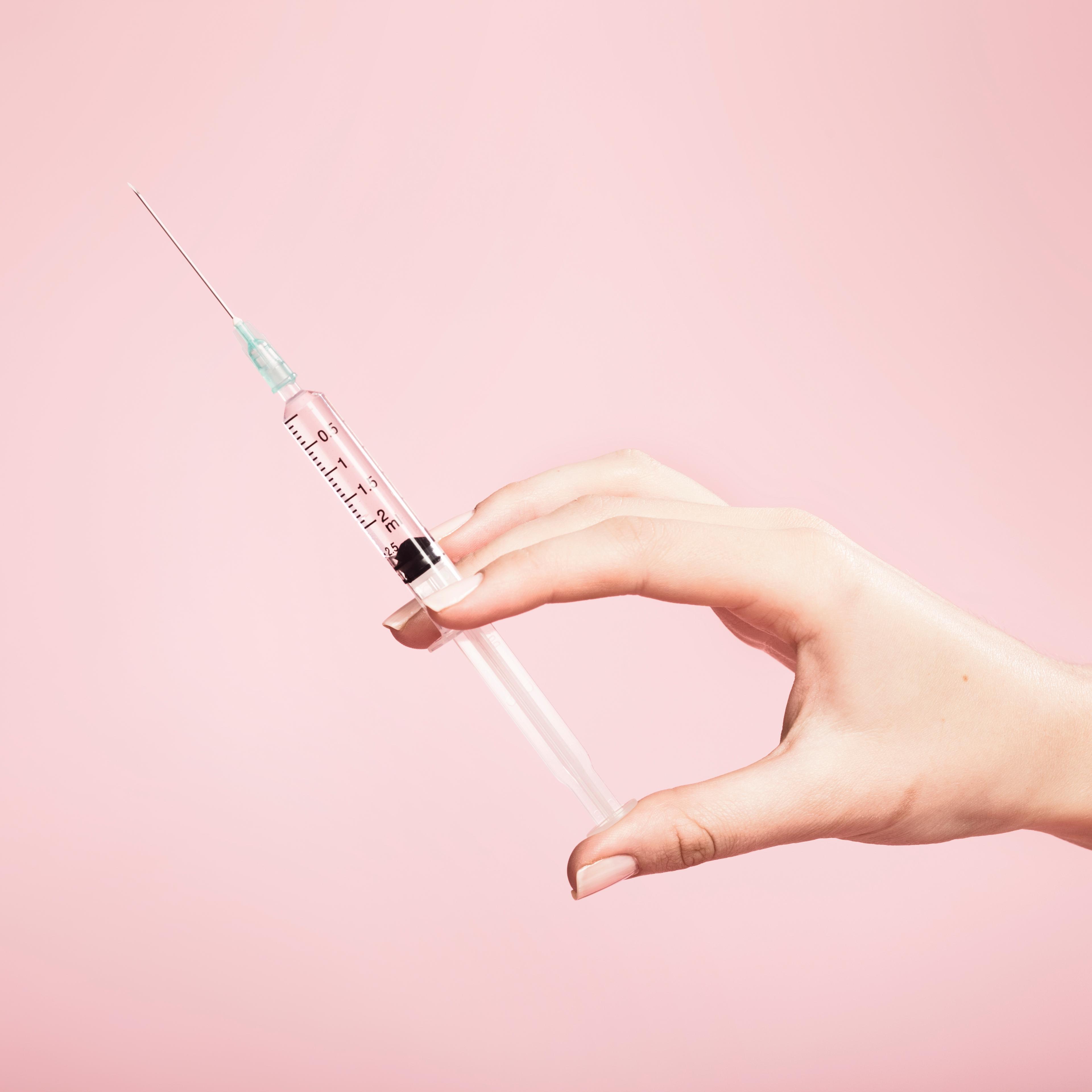 Hand holding syringe in plain pink background TIME health stock