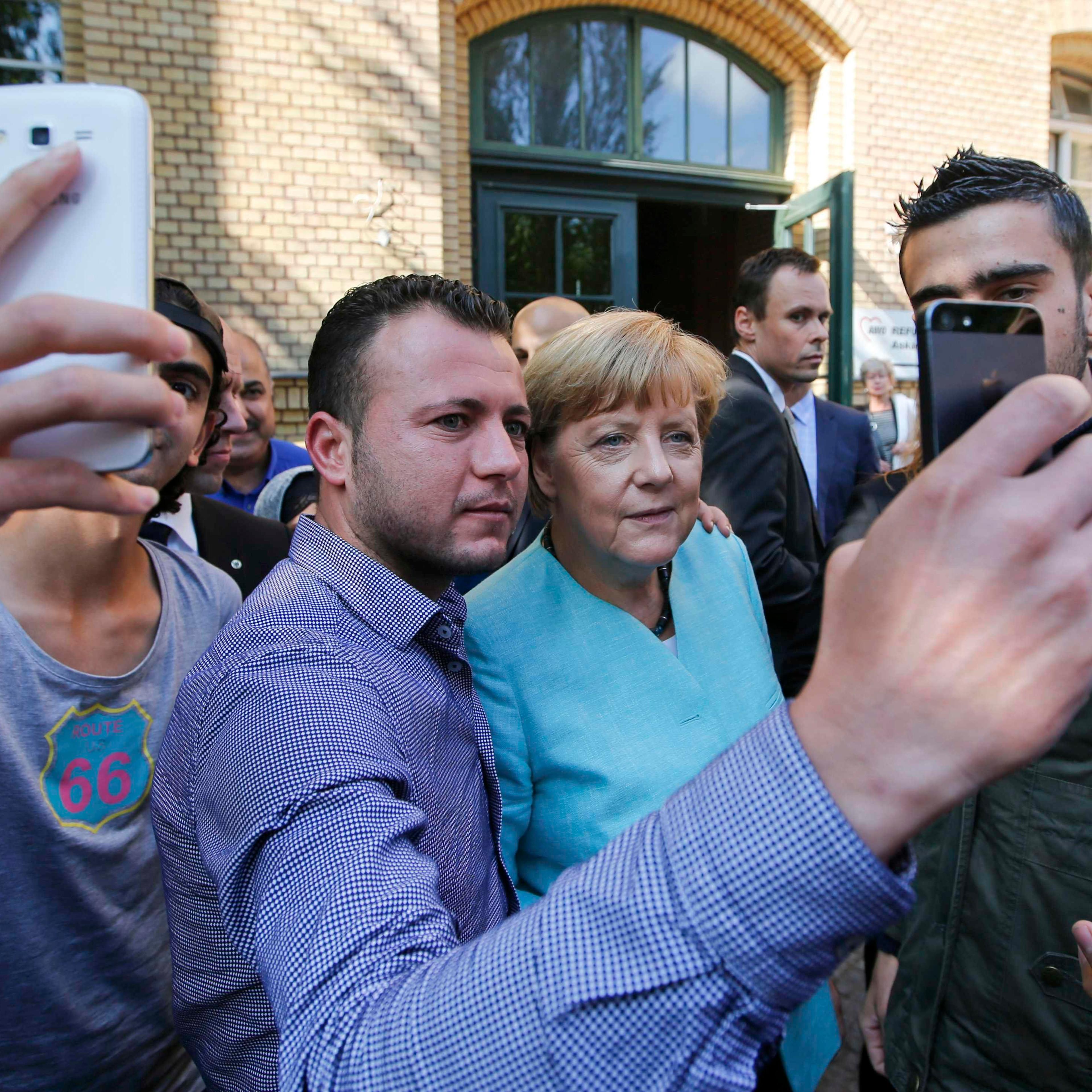 File photo of migrants taking selfies with German Chancellor Merkel outside a refugee camp in Berlin