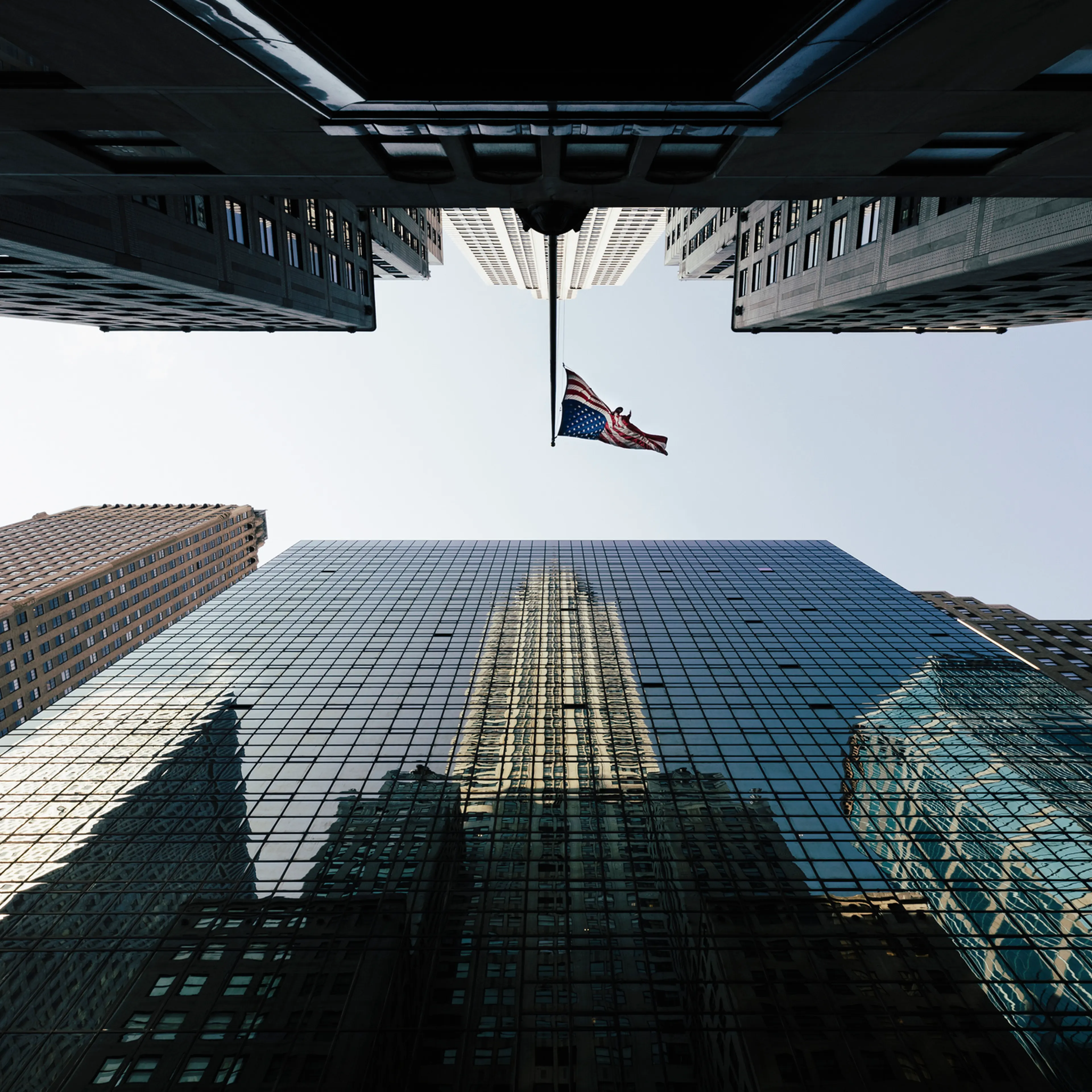 Directly below view of American Flag amidst modern office skyscrapers against sky, New York, USA