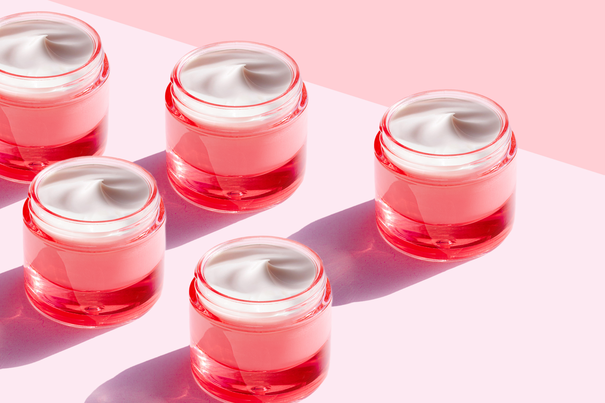 Tubs of moisturizing cream on a pink background.