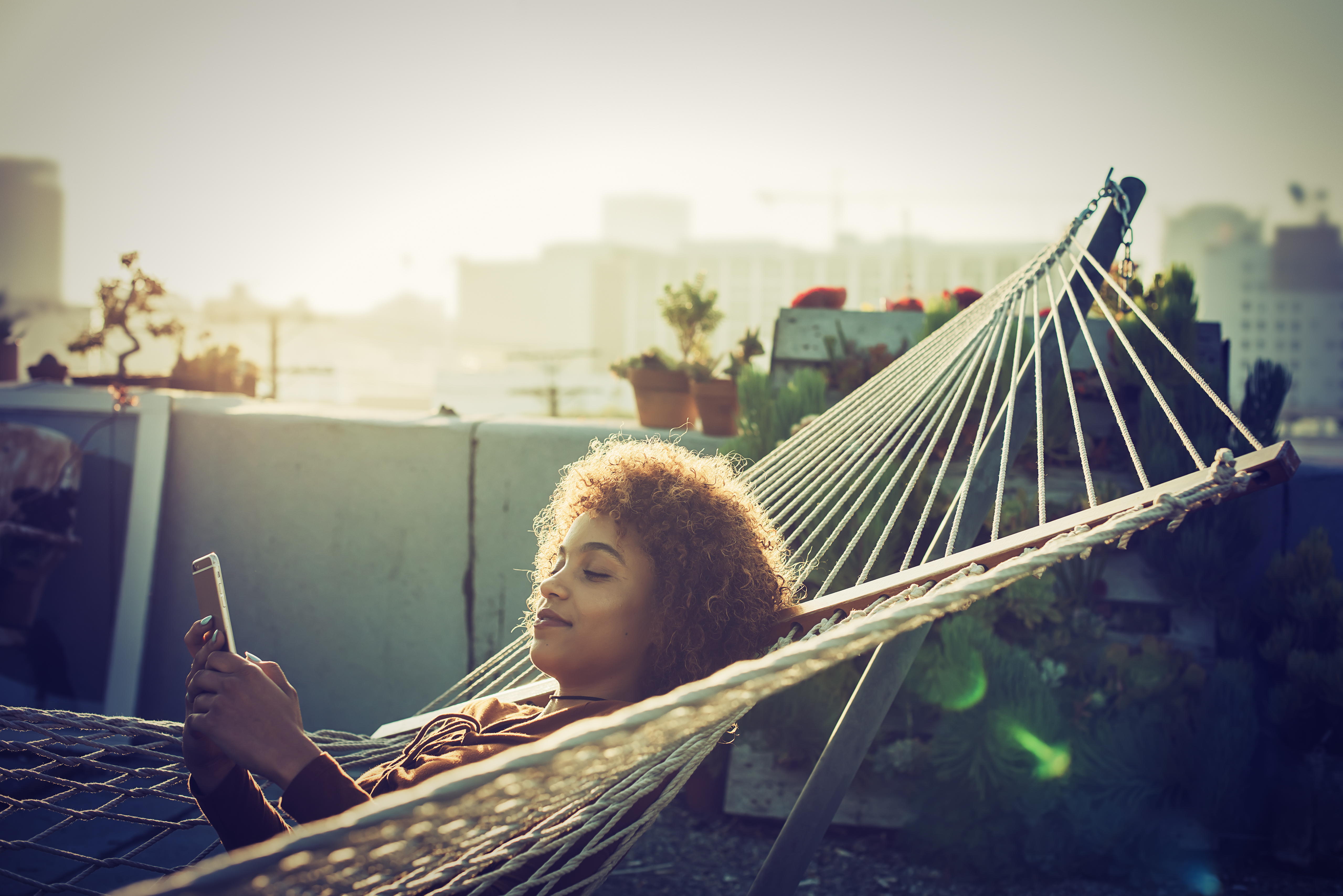 Young woman checks smartphone from hammock