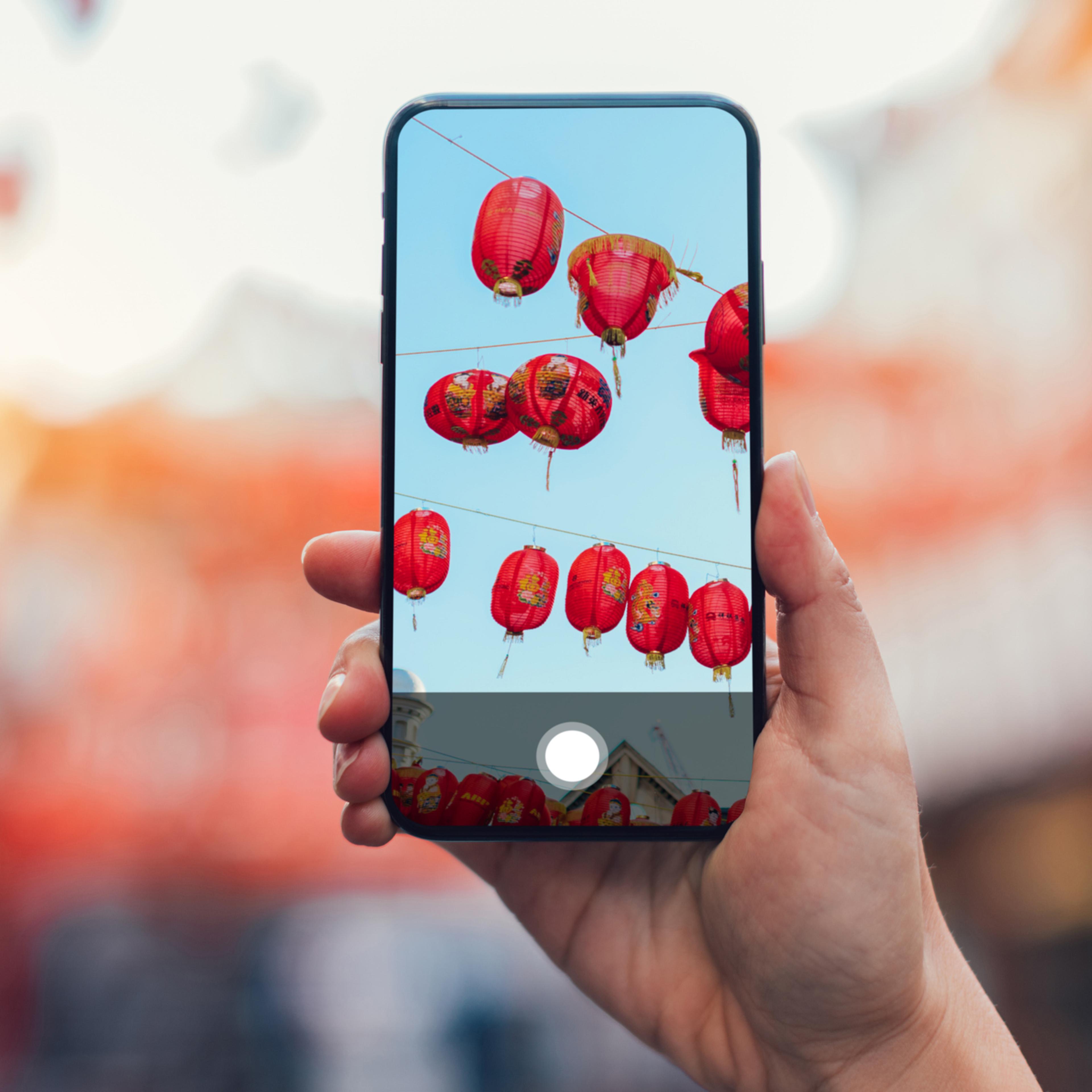 Close-up shot of female hand holding a smartphone, photographing Chinese lantern hanging on the street during Chinese New Year.