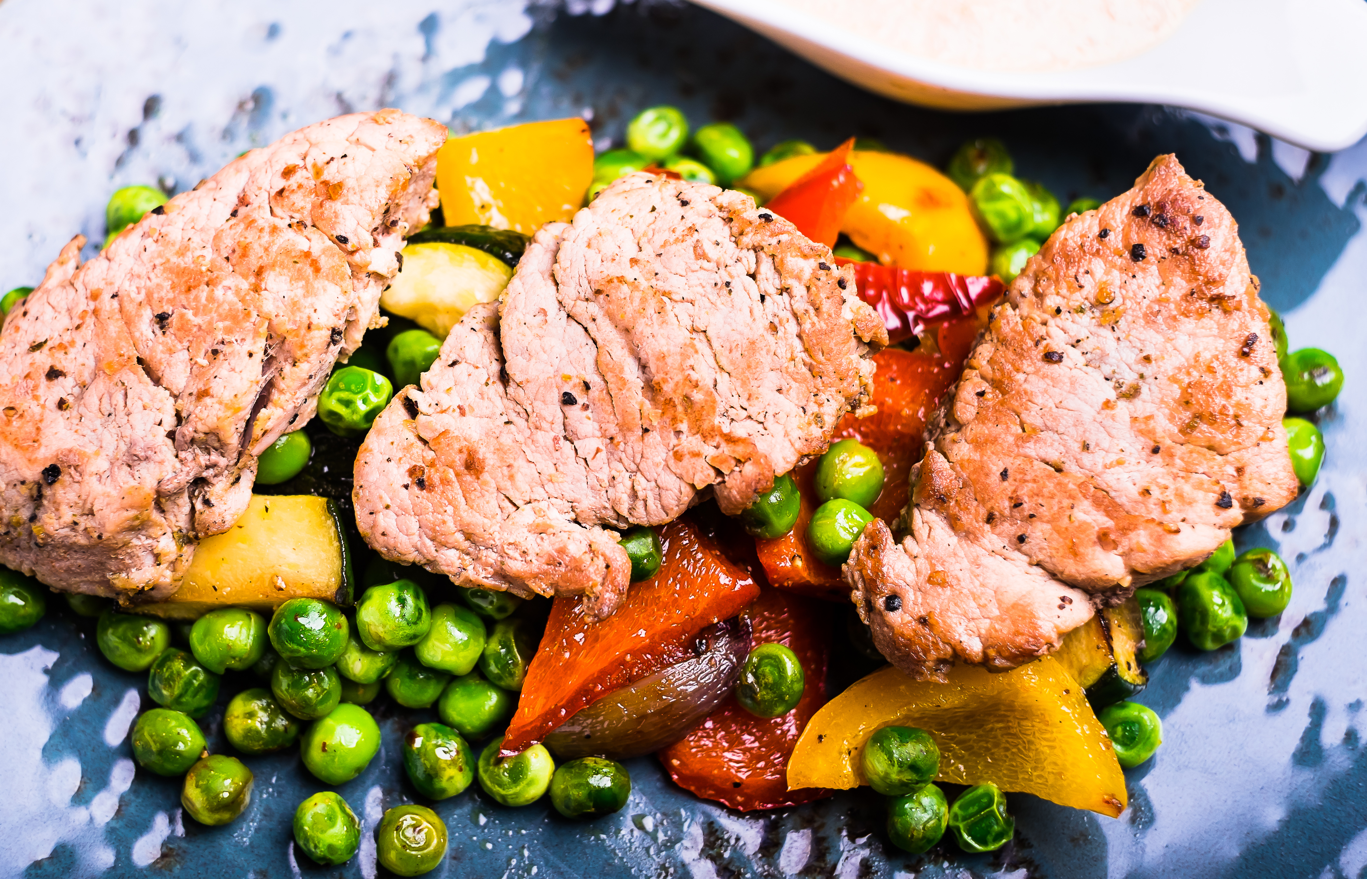 Roasted pork meat fillet chops with zucchini, onion, yellow and orange bell pepper, frozen peas on a plate with cream sauce, top view