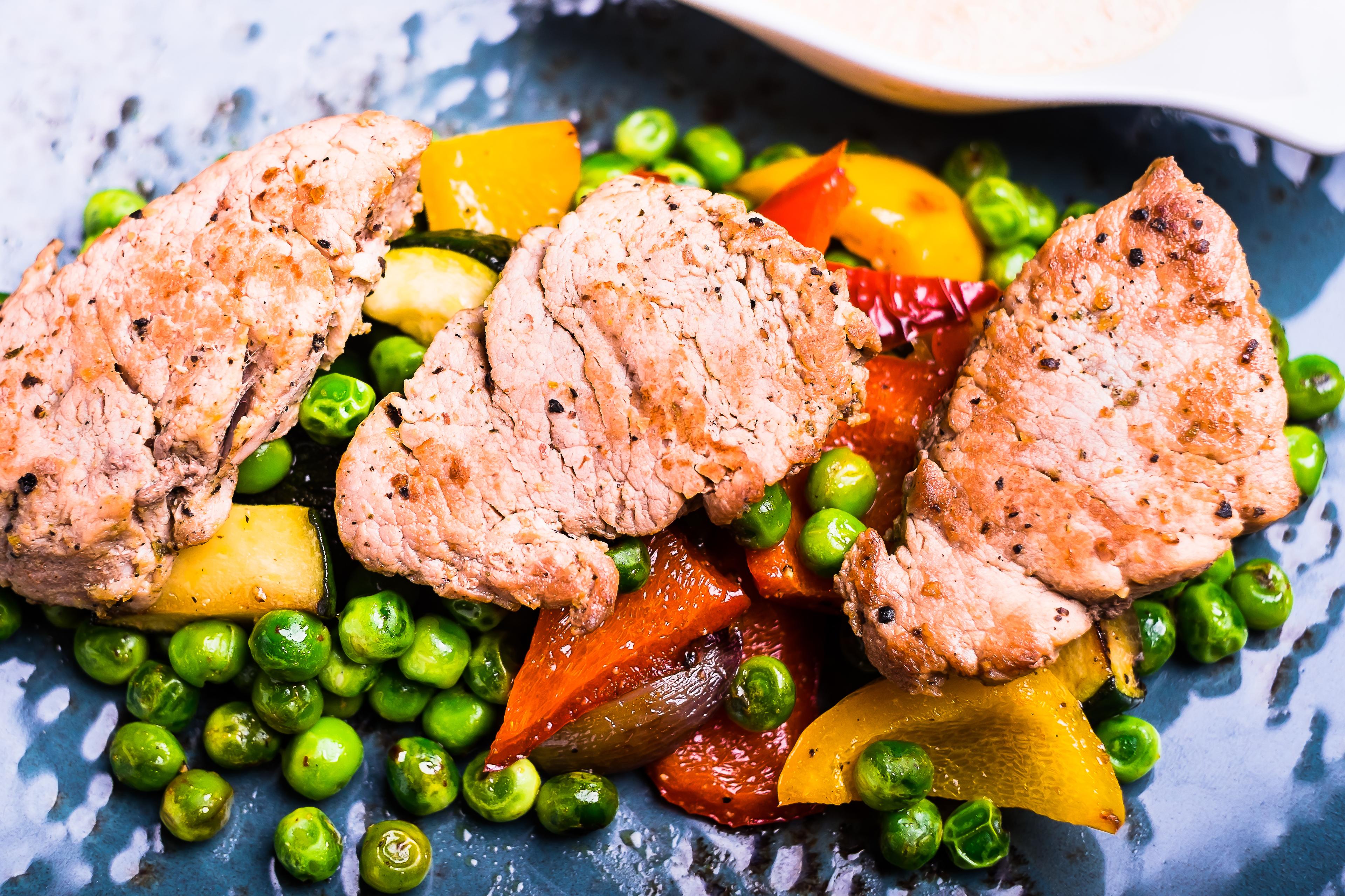 Roasted pork meat fillet chops with zucchini, onion, yellow and orange bell pepper, frozen peas on a plate with cream sauce, top view