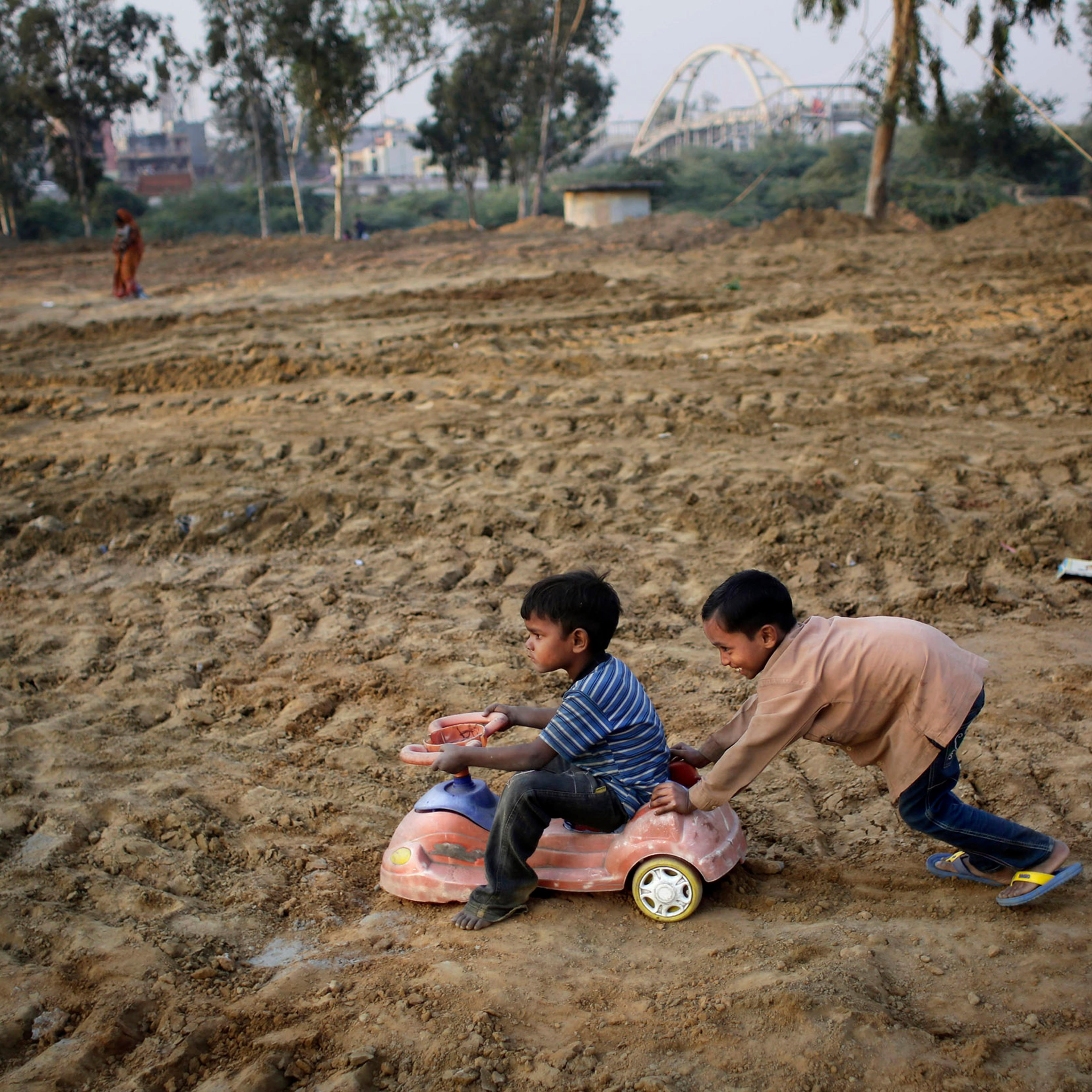 Indian boys play with a toy car salvaged from a nearby landfill in a field being prepared for a metro station near a slum in New Delhi, India on Nov. 13, 2014.