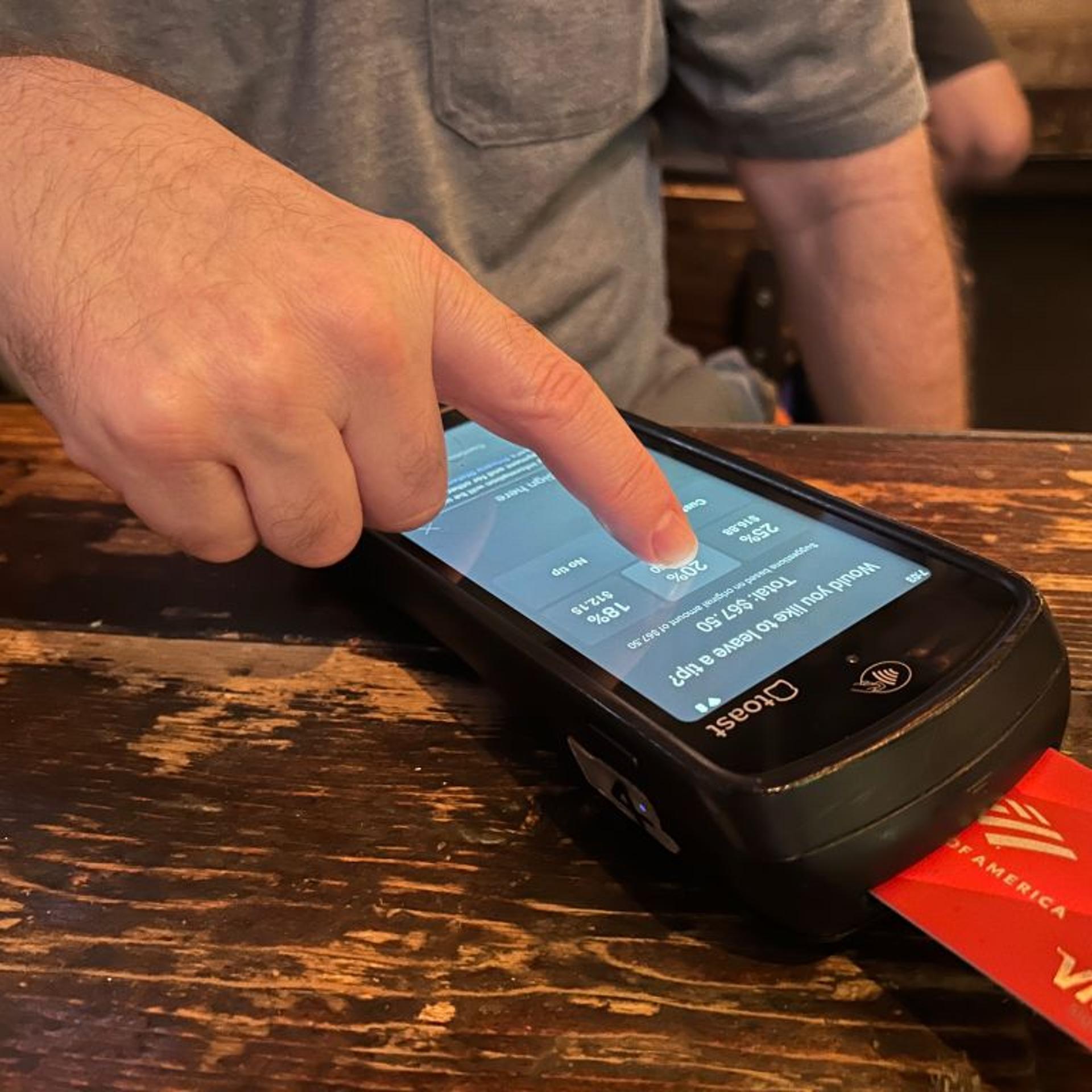 Man selecting 20% tip while using hand held credit card scanner at restaurant, Queens, New York