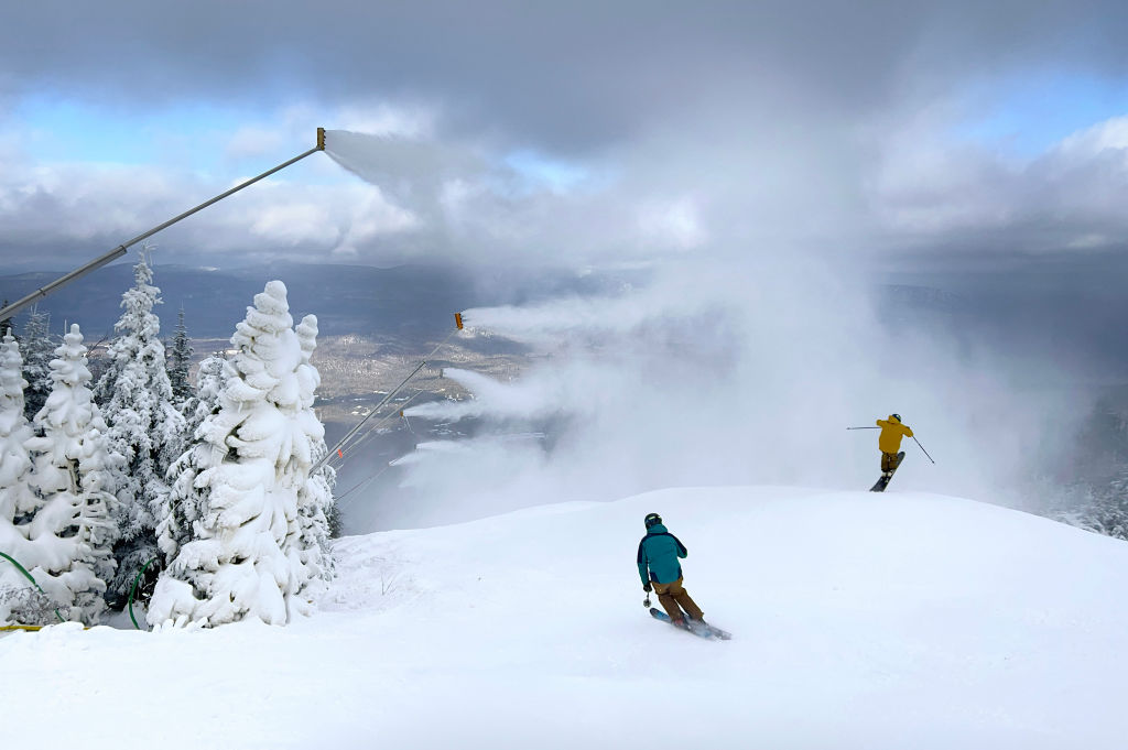 Snow guns blow snow over skiers as they make their way down the hill.