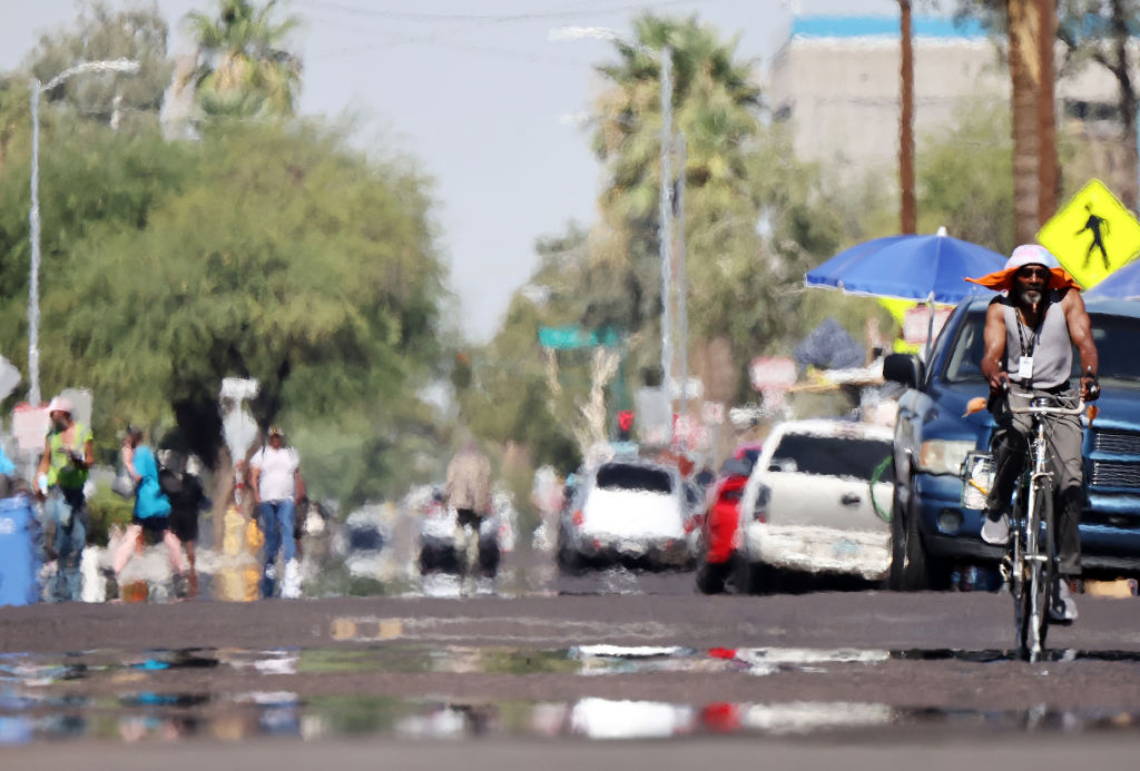 A person rides a bicycle as heat waves shimmer, causing visual distortion, as people walk in the 'The Zone', Phoenix's largest homeless encampment, amid the city's worst heat wave on record on July 25, 2023 in Phoenix, Arizona.
