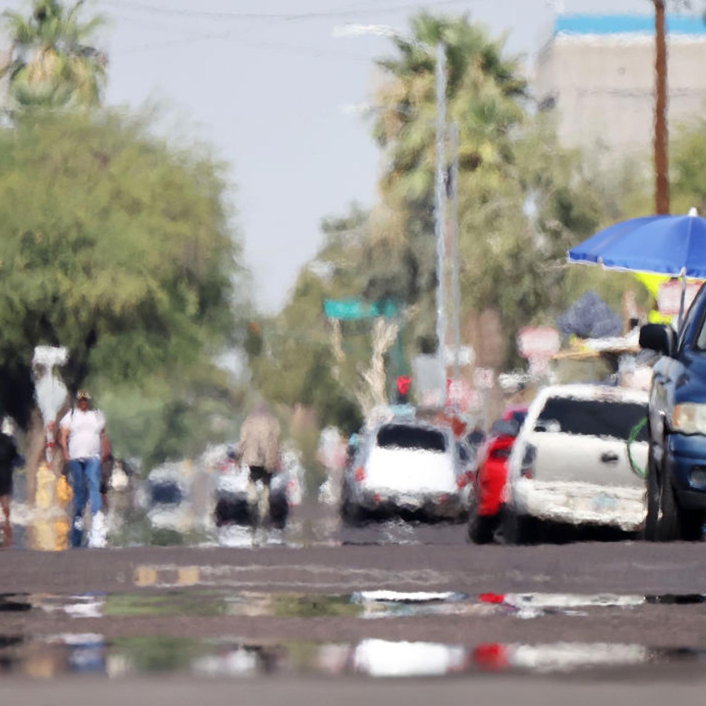 A person rides a bicycle as heat waves shimmer, causing visual distortion, as people walk in the 'The Zone', Phoenix's largest homeless encampment, amid the city's worst heat wave on record on July 25, 2023 in Phoenix, Arizona.