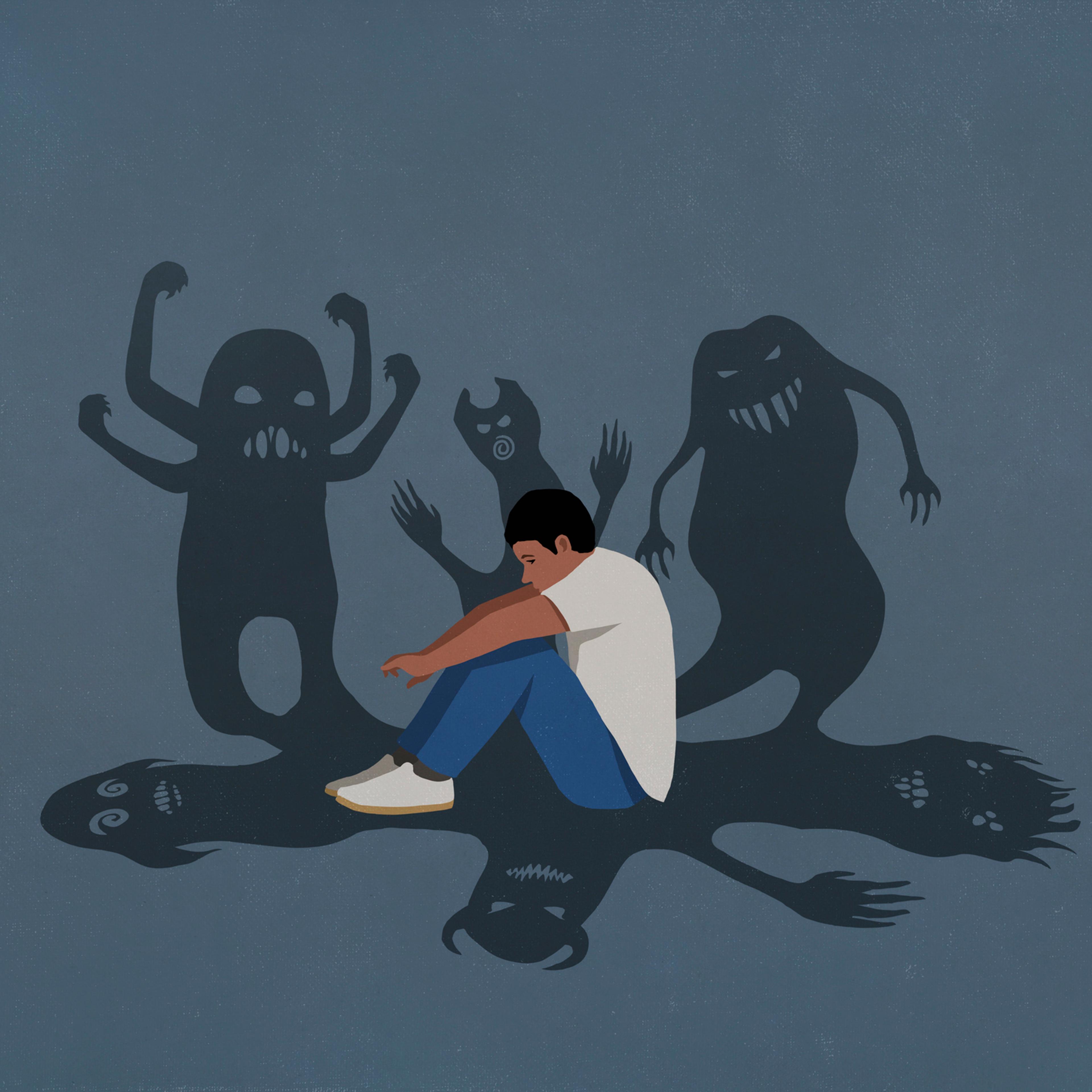 Shadows of monsters surrounding anxious teenage boy hugging knees
