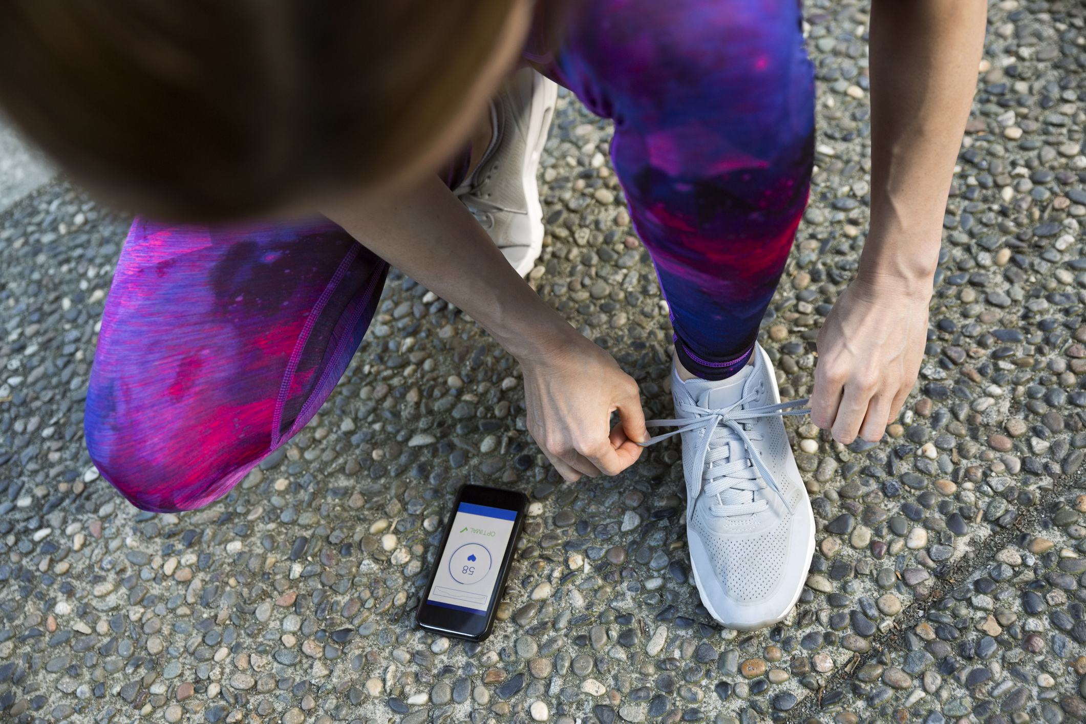 Runner tying shoe and checking heart rate app on cell phone