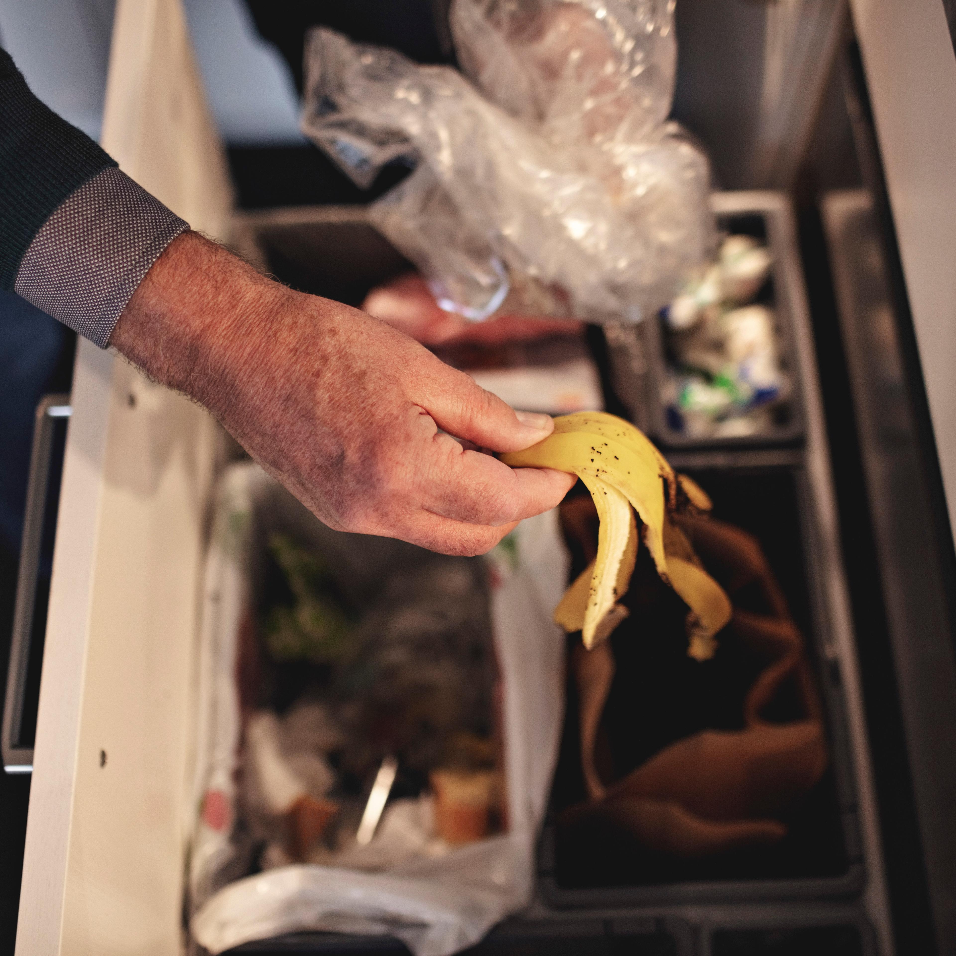Cropped hand of senior man throwing garbage in dustbin at home