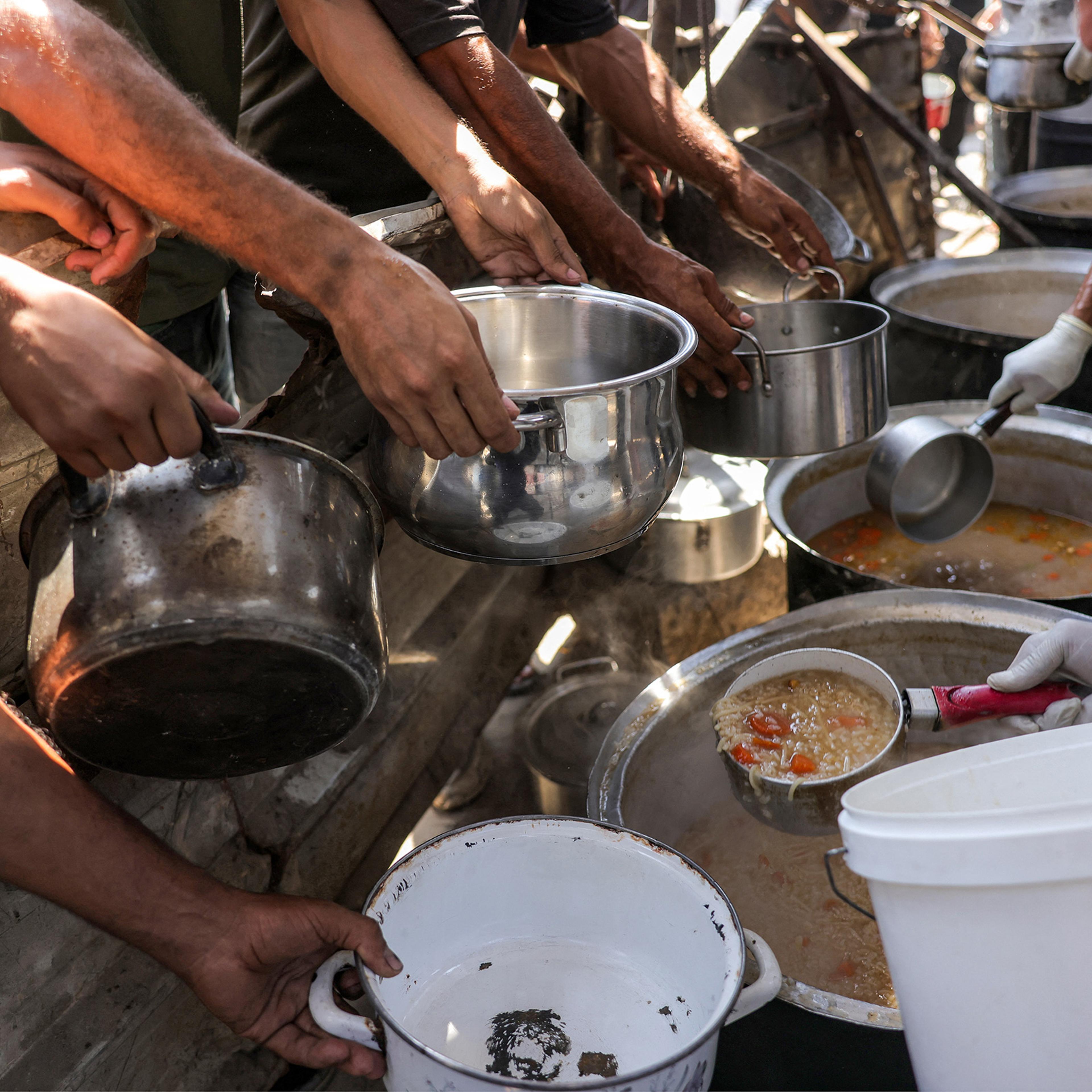 People queue with pots to receive meals from a charity kitchen in Gaza City on July 14, 2025.