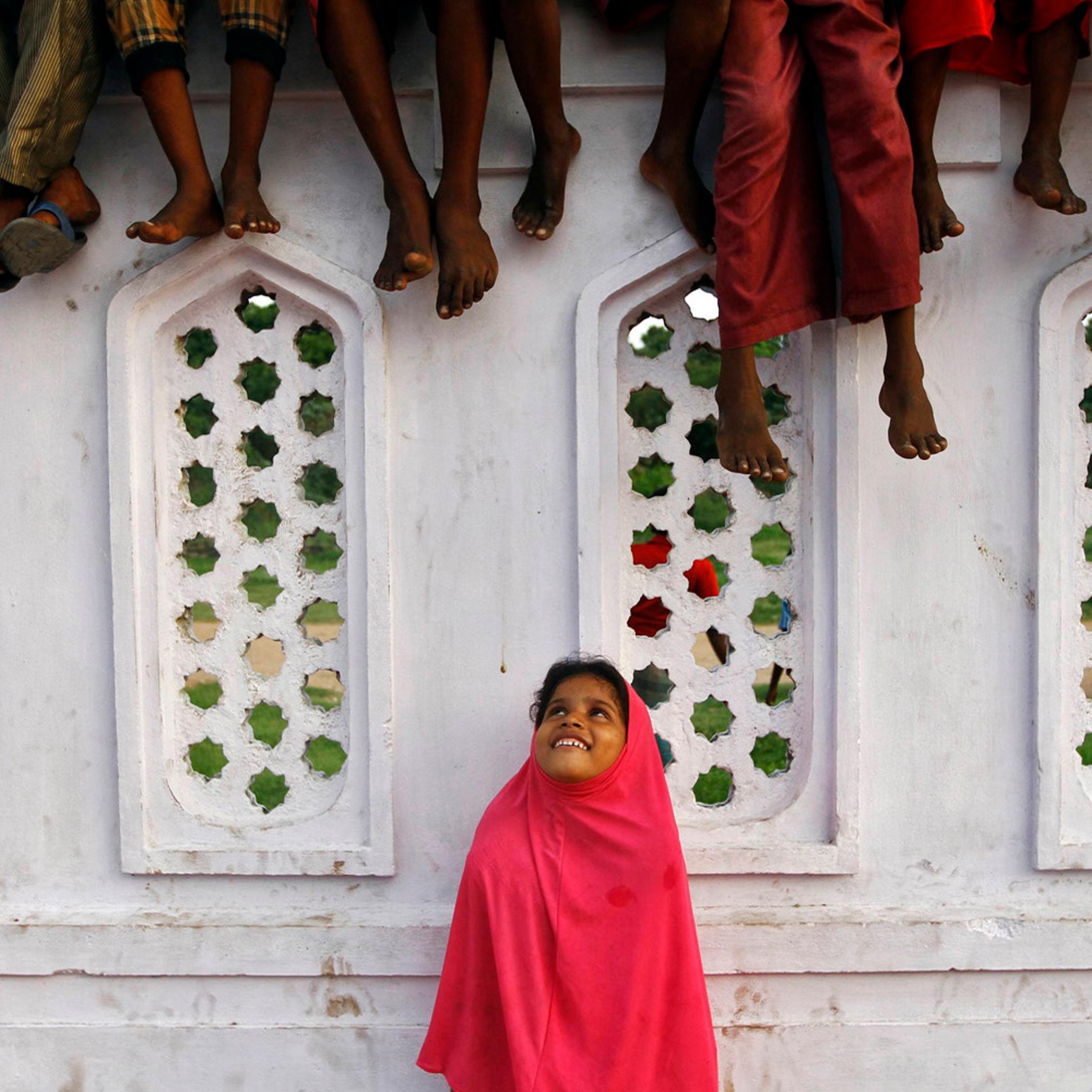 A Muslim girl looks up while some boys sit on a wall, inside the premises of a mosque, as they wait for Iftar (breaking fast) meal during the holy month of Ramadan in the southern Indian city of Chennai