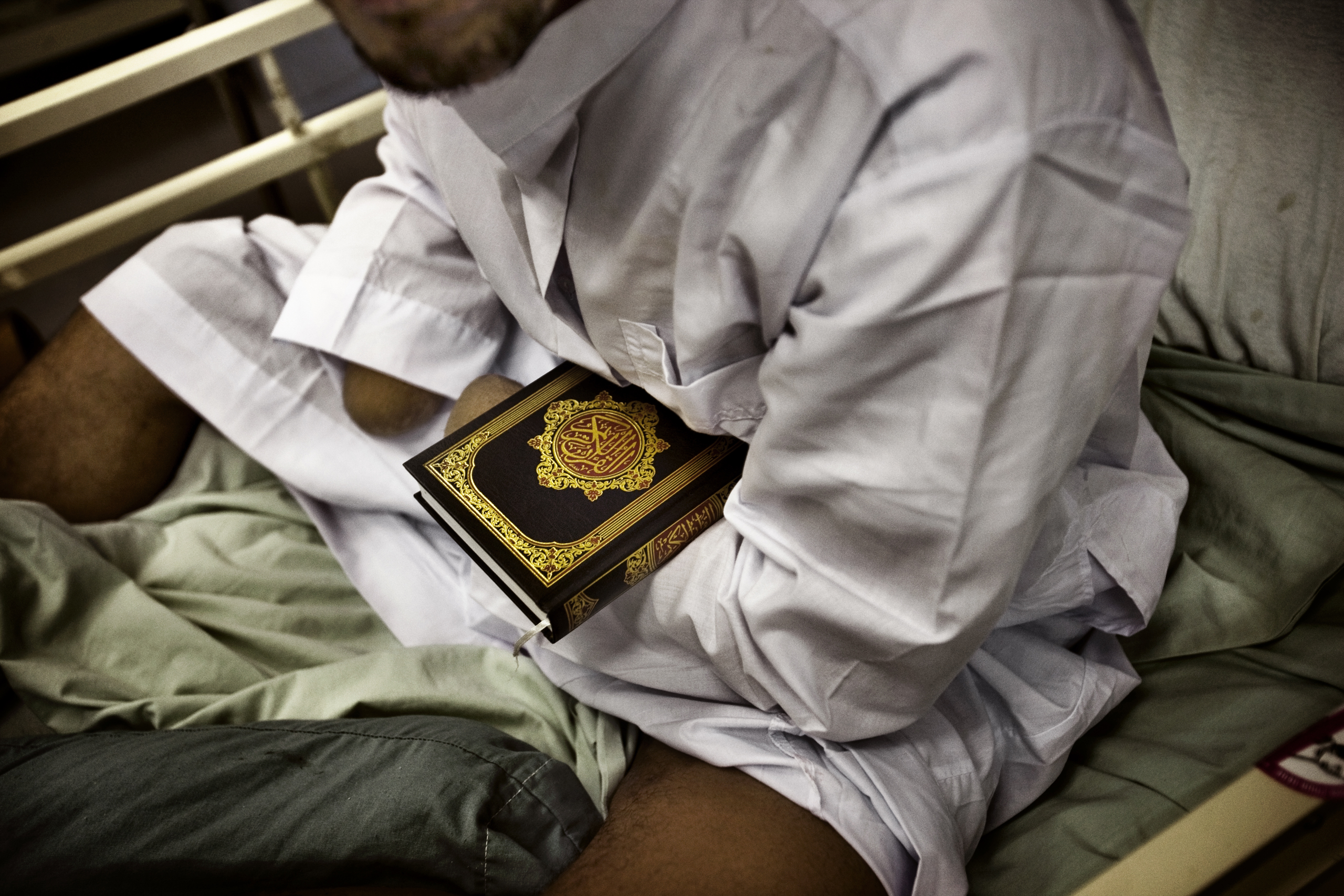 A detainee patient, who nurses say likely lost his hands while handling explosives, holds a Quran at the hospital at Camp Cropper, a U.S. military detention facility in Baghdad, July 26, 2008.