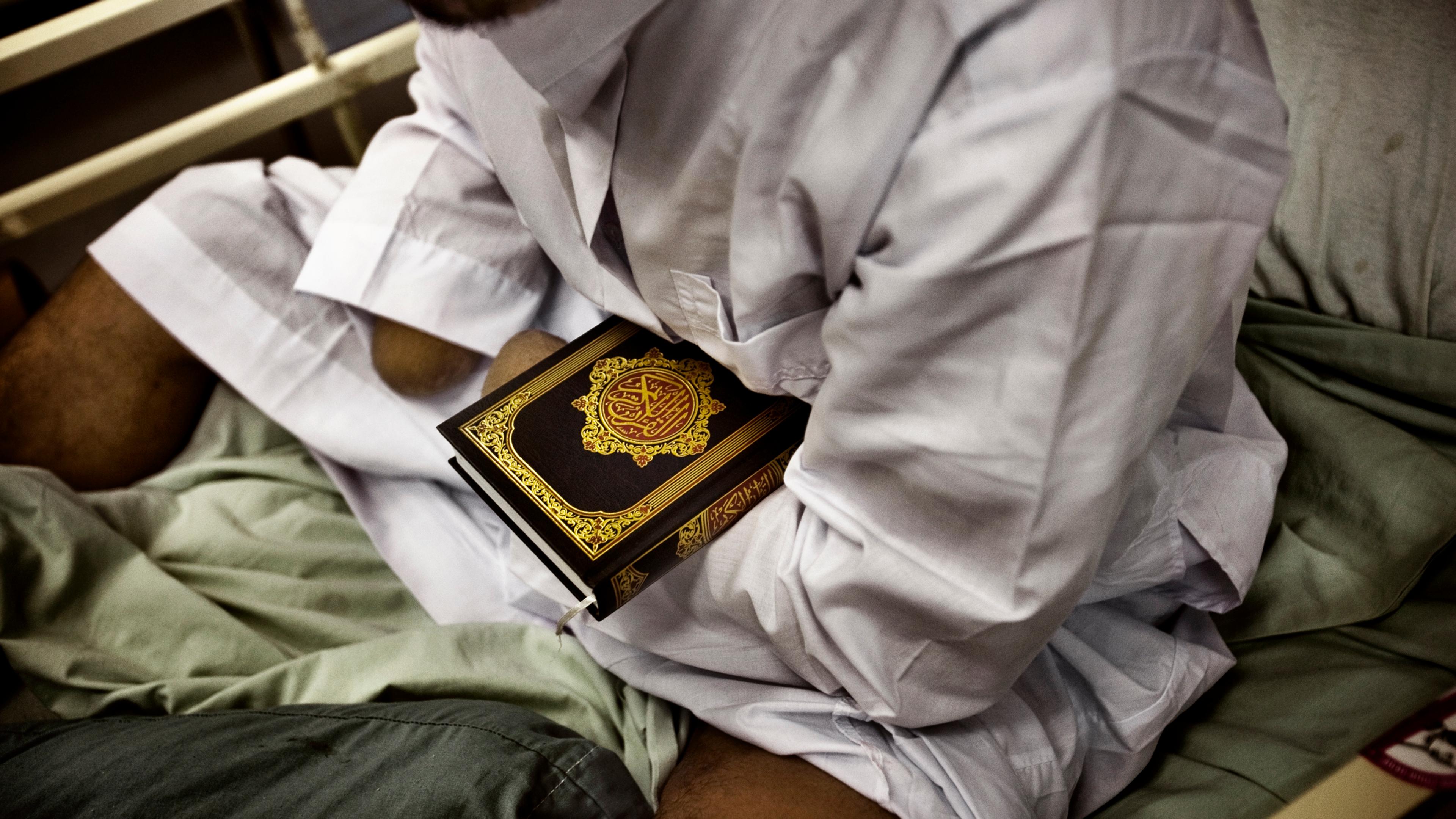 A detainee patient, who nurses say likely lost his hands while handling explosives, holds a Quran at the hospital at Camp Cropper, a U.S. military detention facility in Baghdad, July 26, 2008.