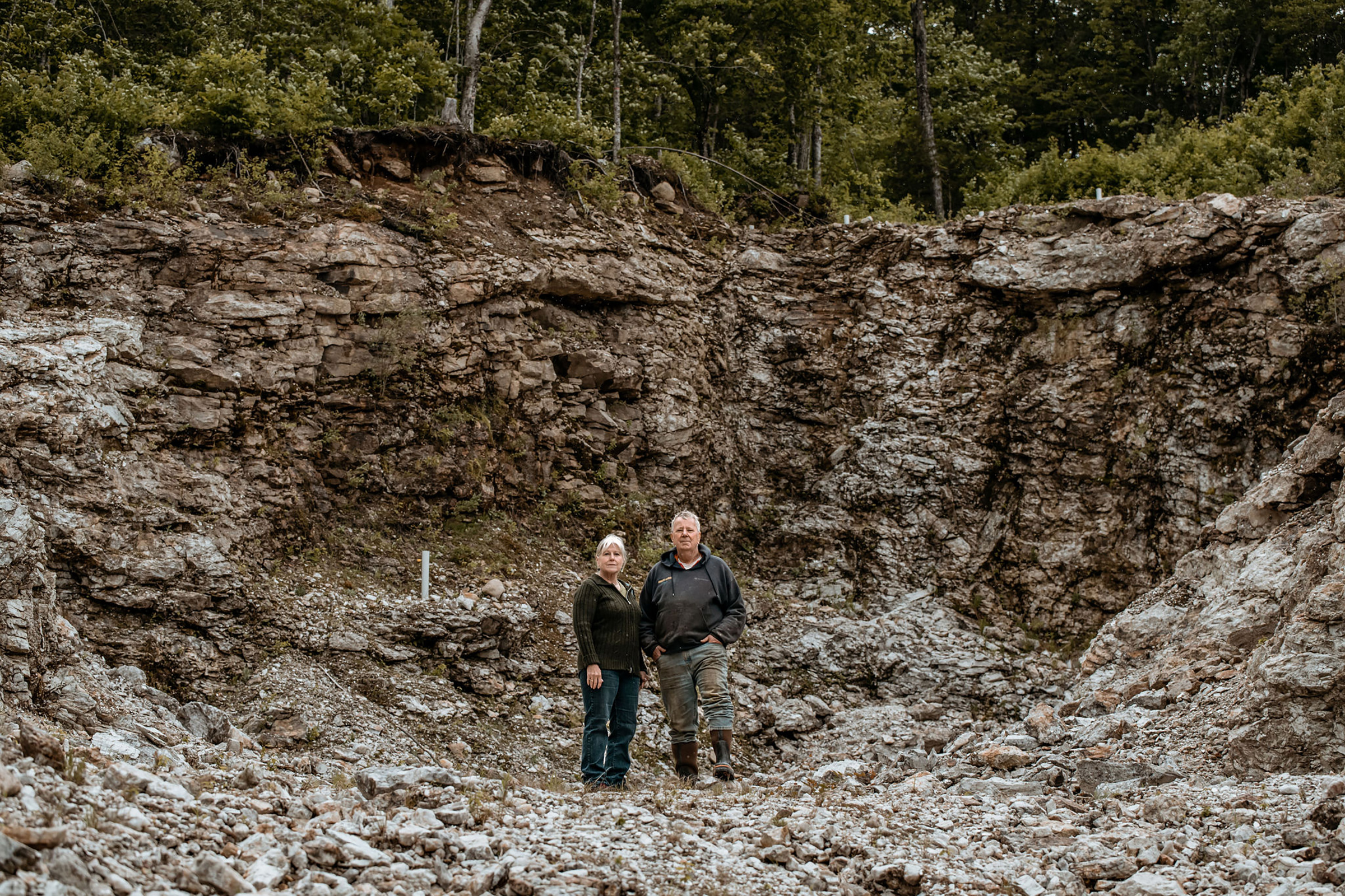Mary and Gary Freeman stand in a pit in Newry, Maine, where they have excavated 700 tons of the lithium-bearing mineral spodumene under an exploratory permit, on June 6. The site, also known as Plumbago North, contains some of the largest specimens of  spodumene ever uncovered, with some measuring up to 36 feet in length. The state of Maine currently bars them from further extracting the rock. 