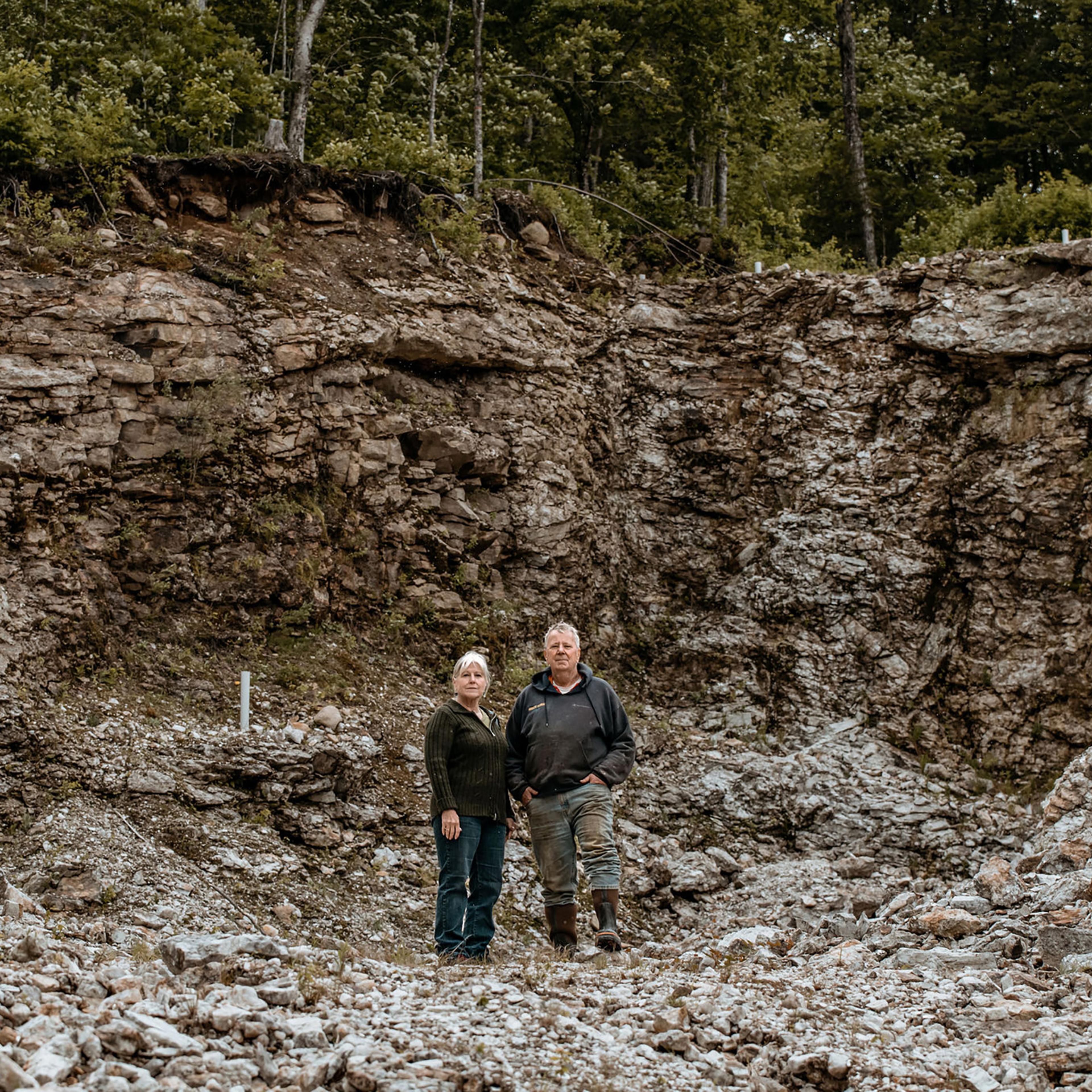 Mary and Gary Freeman stand in a pit in Newry, Maine, where they have excavated 700 tons of the lithium-bearing mineral spodumene under an exploratory permit, on June 6. The site, also known as Plumbago North, contains some of the largest specimens of spodumene ever uncovered, with some measuring up to 36 feet in length. The state of Maine currently bars them from further extracting the rock.