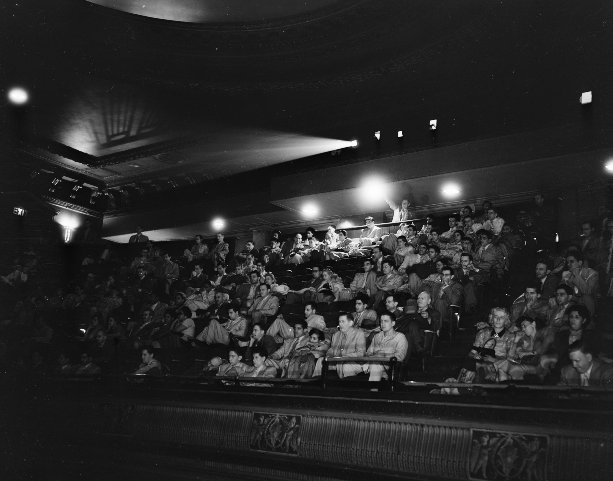 A projection beam cuts throught the darkness of a 1940s cinema interior