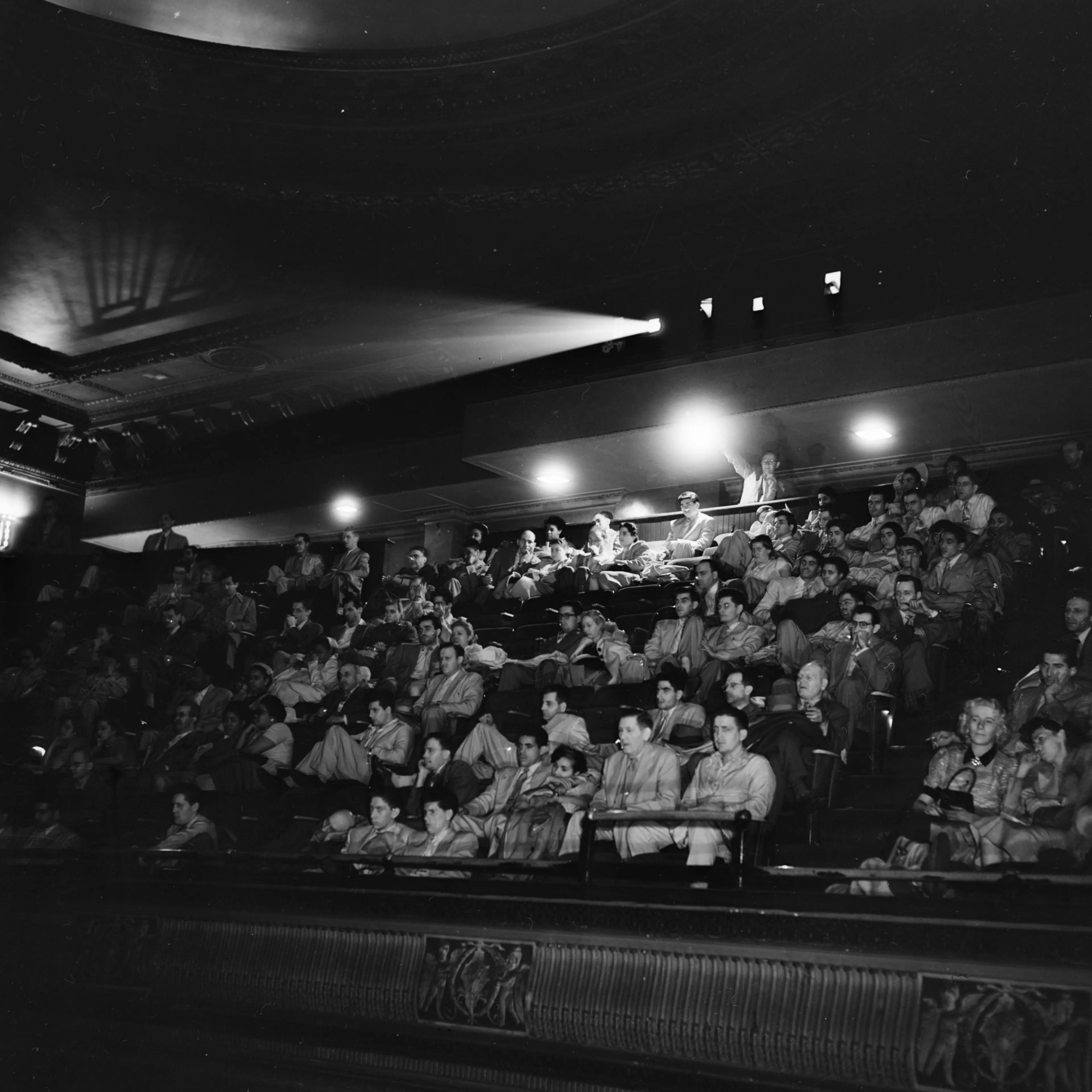 A projection beam cuts throught the darkness of a 1940s cinema interior