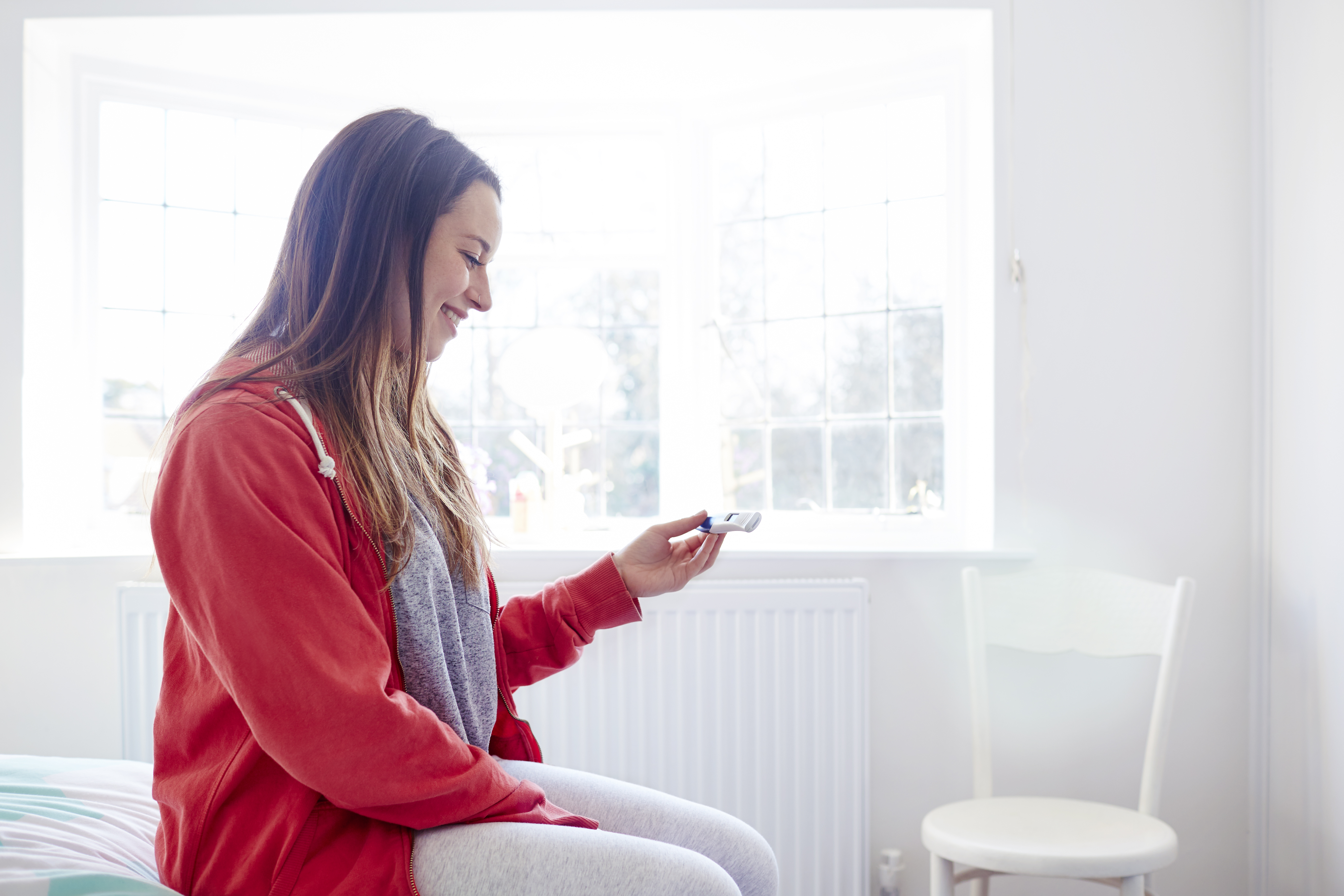 Woman sitting on bed looking at pregnancy test
