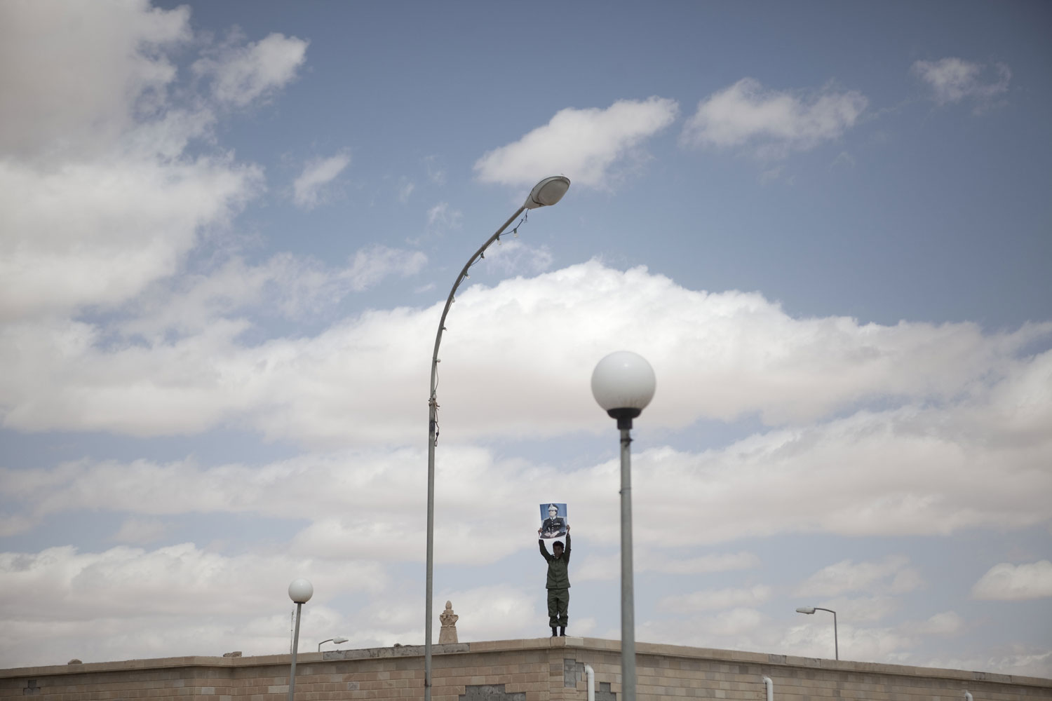 A supporter of Libyan leader Muammar Gaddafi holds a poster overlooking a demonstration in Ban-Waled, March 23, 2011.