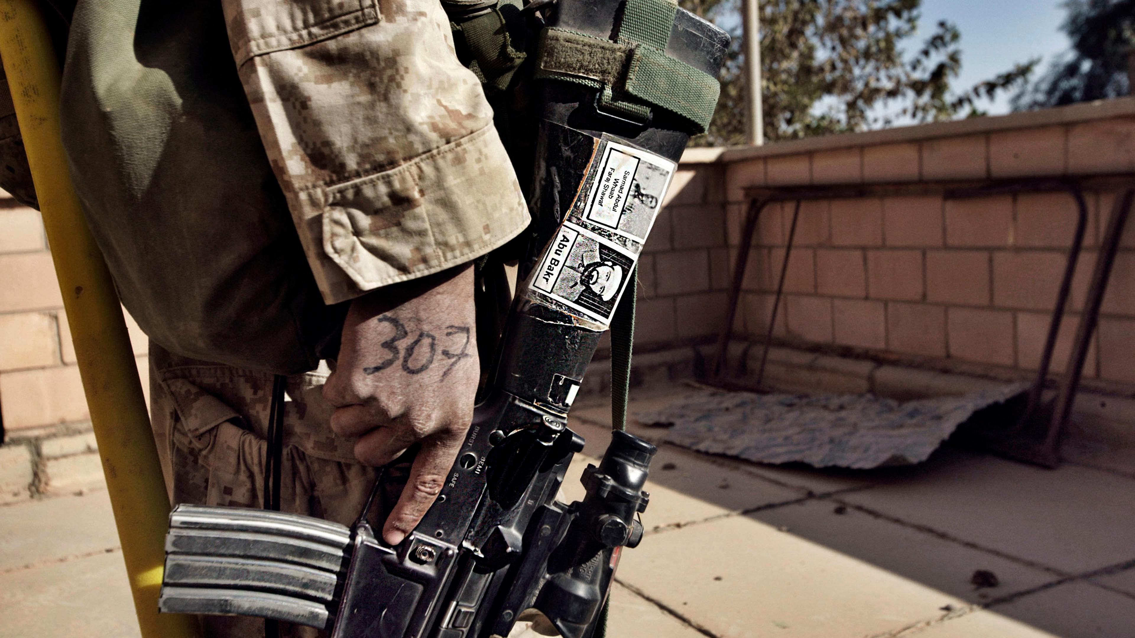 A Marine from Fox Co. 2nd Battalion 1st Marines holds his M-16 rifle with pictures of suspected insurgents during the first day of Operation Steel Curtain, an effort to stop foreign fighters from crossing into Iraq. Nov. 5, 2005.
