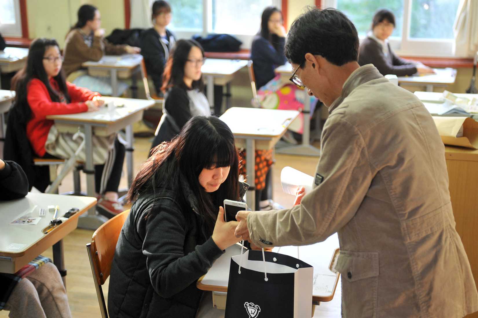 An examination invigilator (R) collects mobile phones from South Korean students before they take the College Scholastic Ability Test, a standardised exam for college entrance, at a high school in Seoul on November 7, 2013.