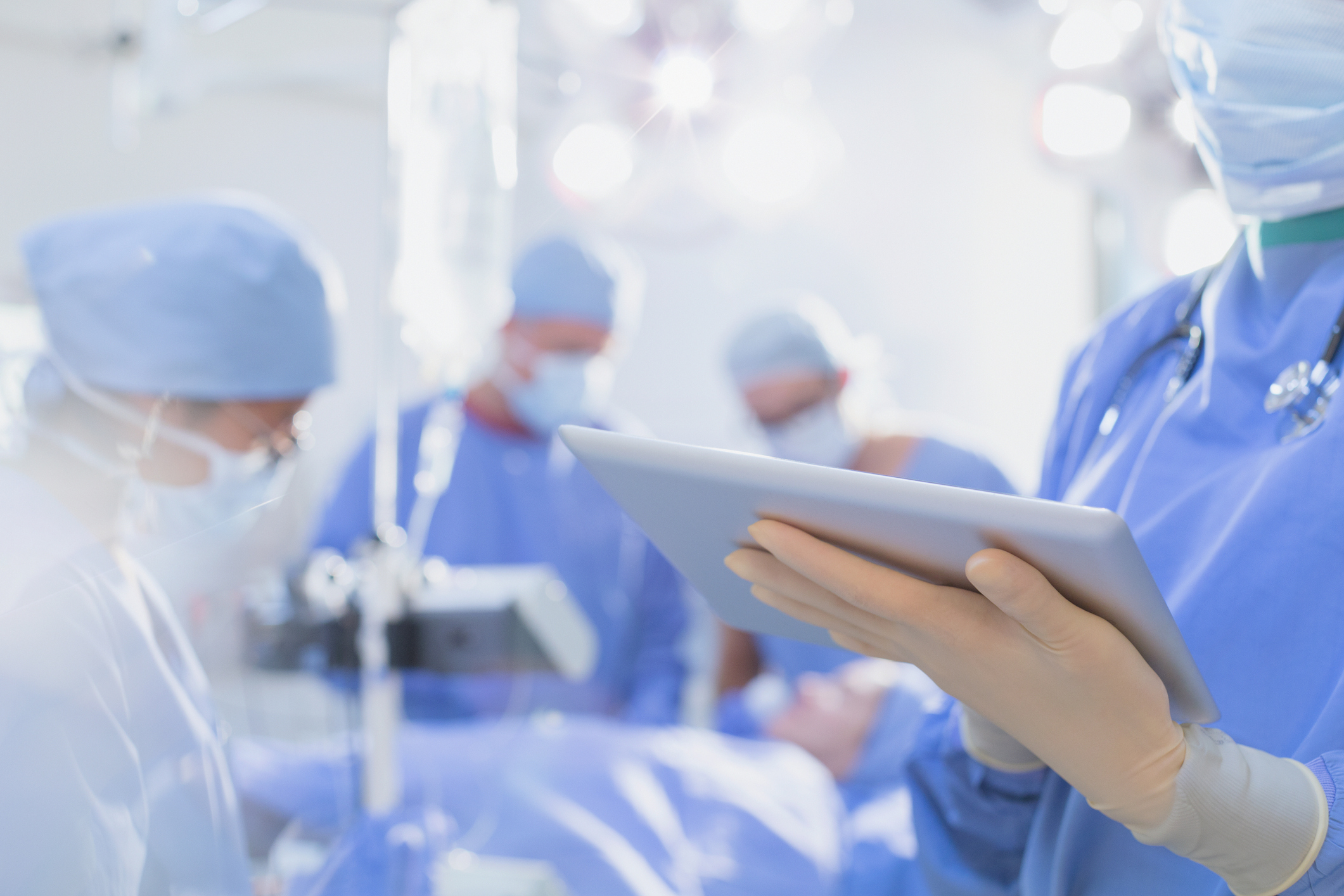 Surgeon wearing rubber gloves, using digital tablet in operating room