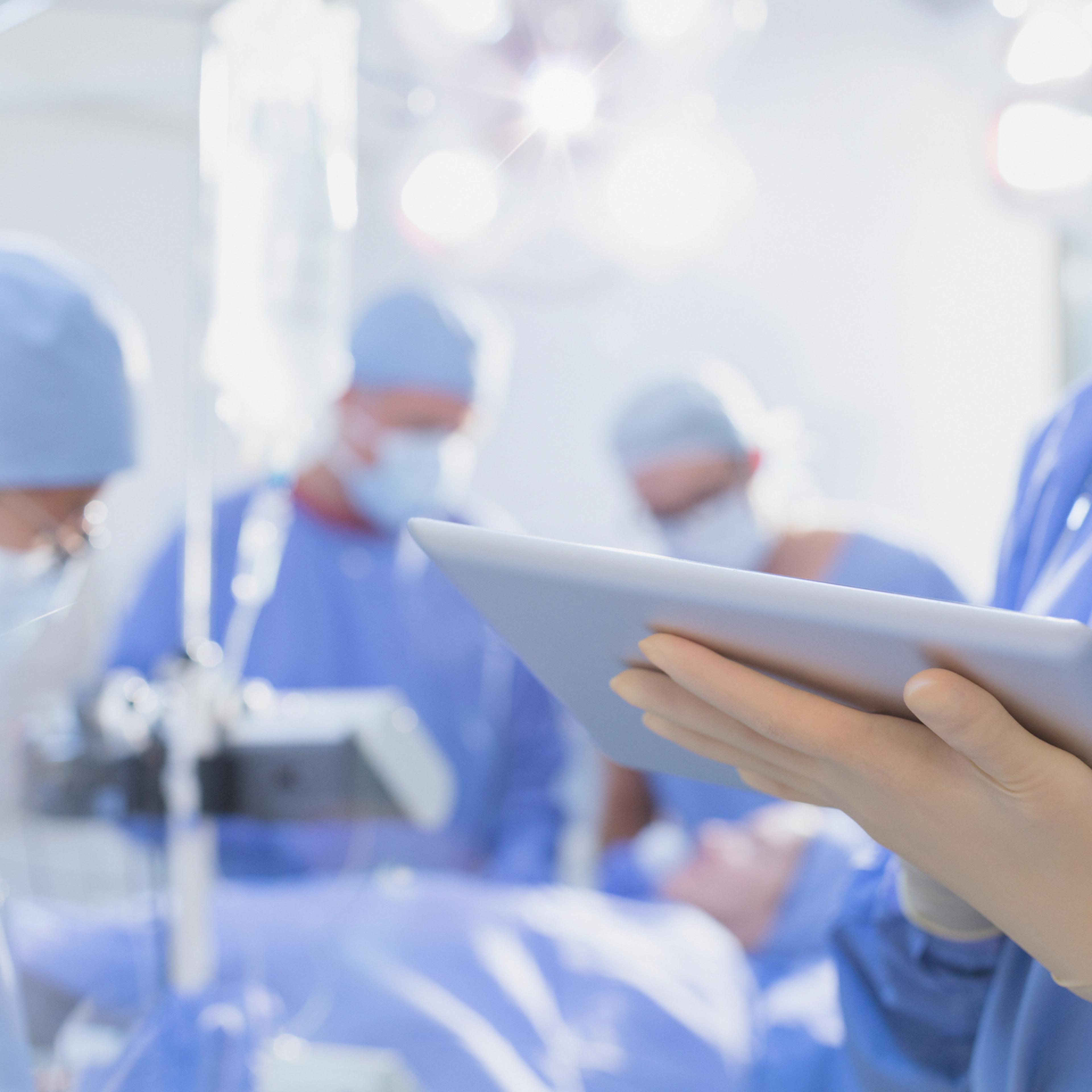 Surgeon wearing rubber gloves, using digital tablet in operating room