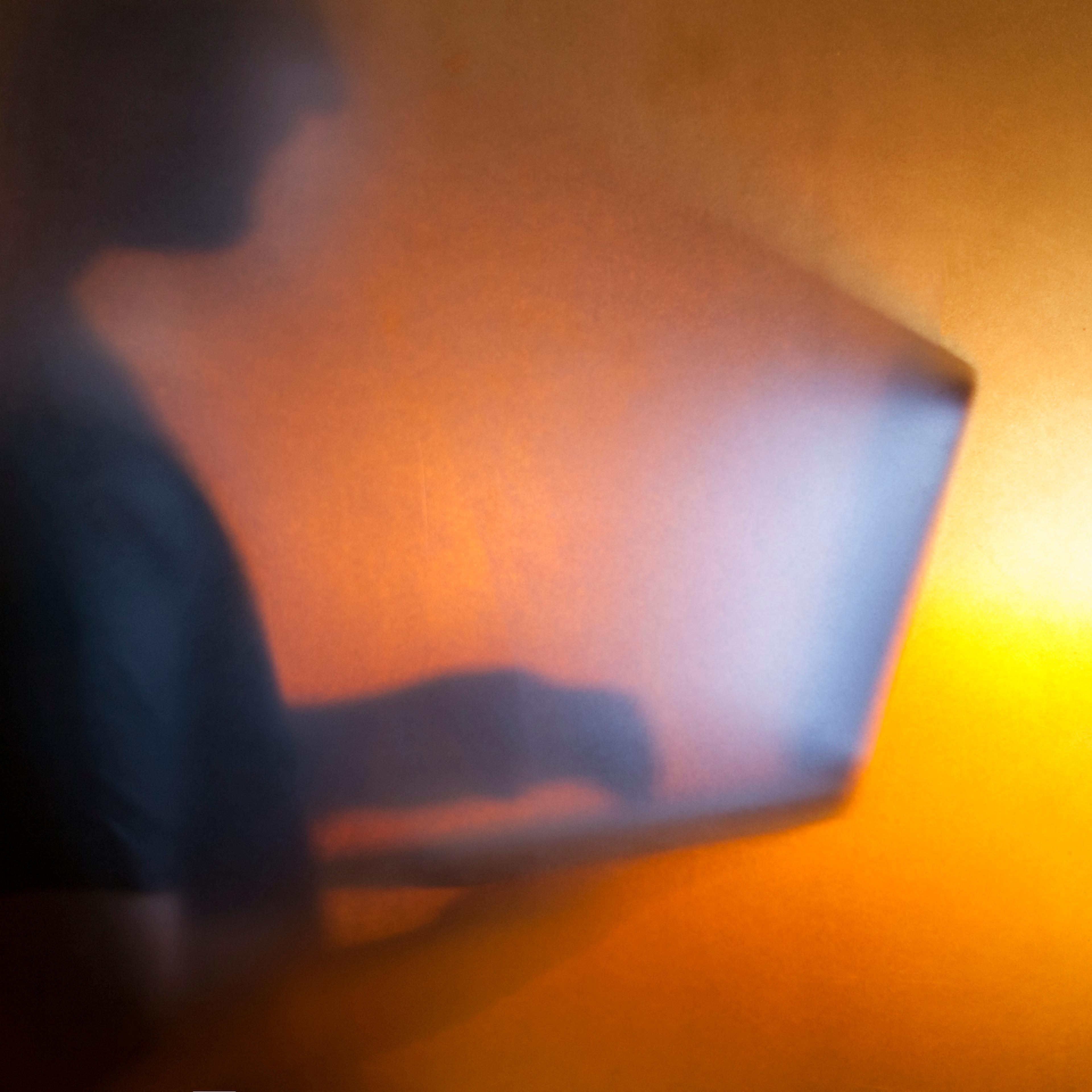 Man using laptop behind translucent glass with warm background