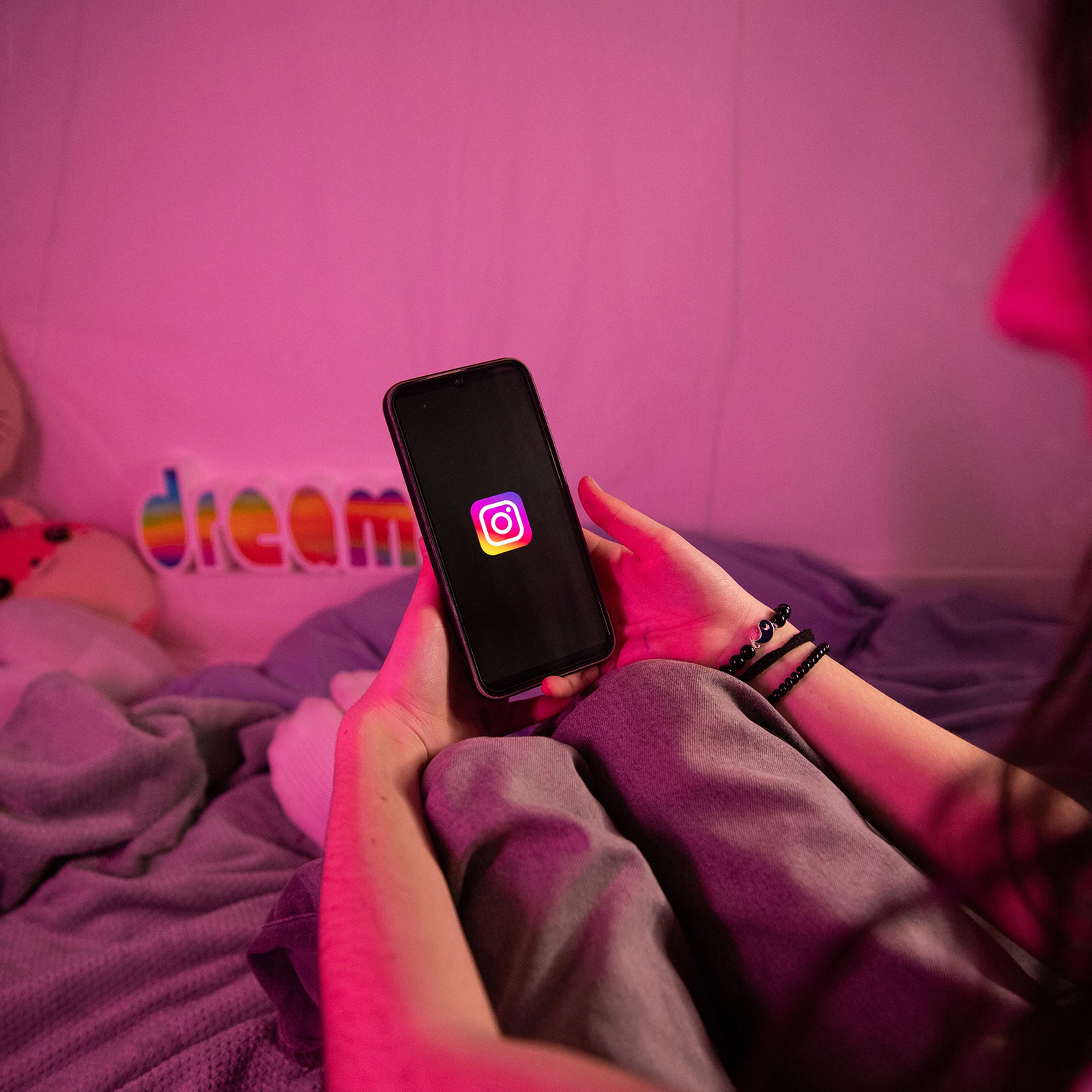 A teenager holds a phone whose screen displays the Instagram social media logo.