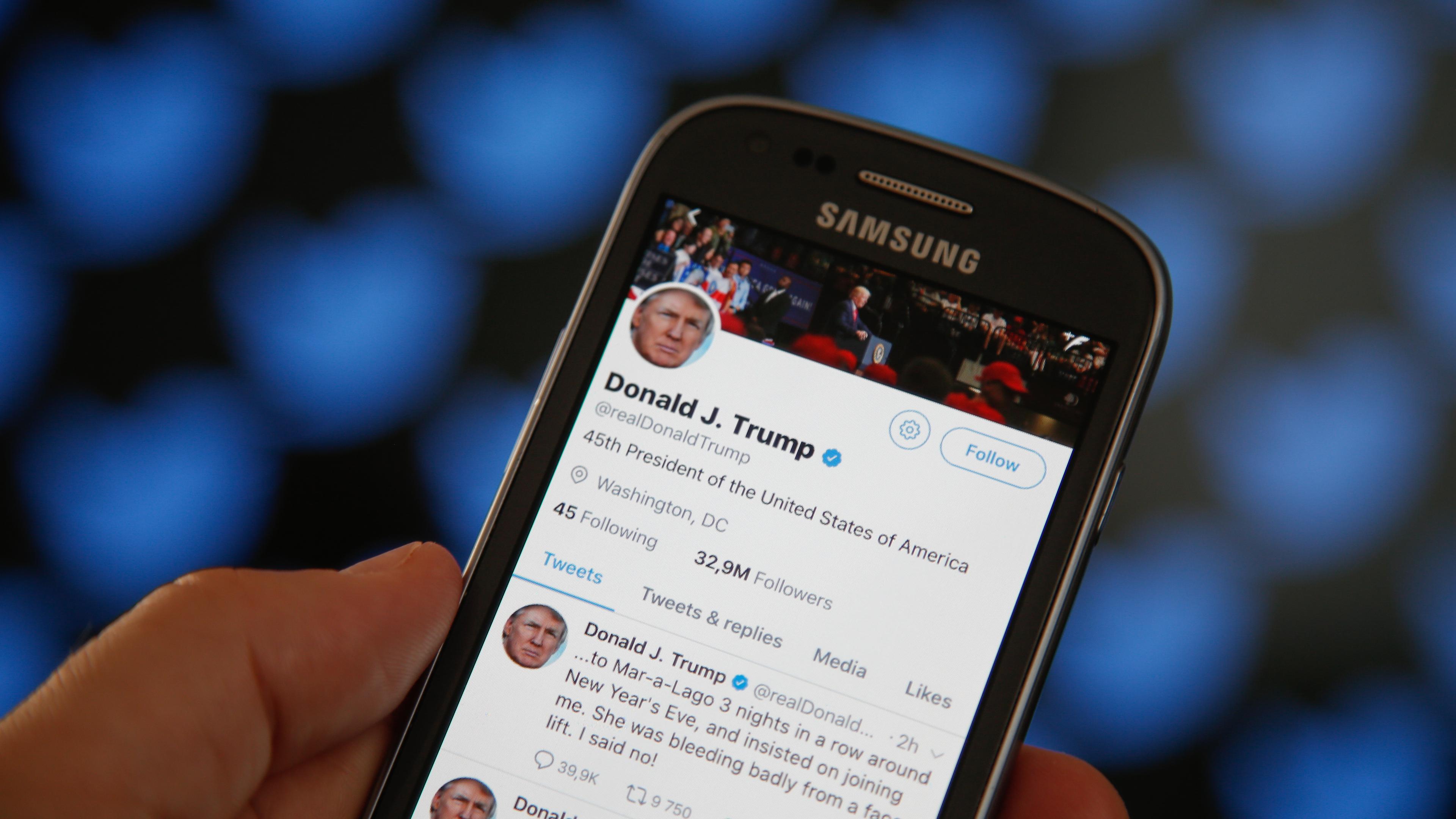 Trump's twitter timeline in front of a screen with the Twitter logo in a patten