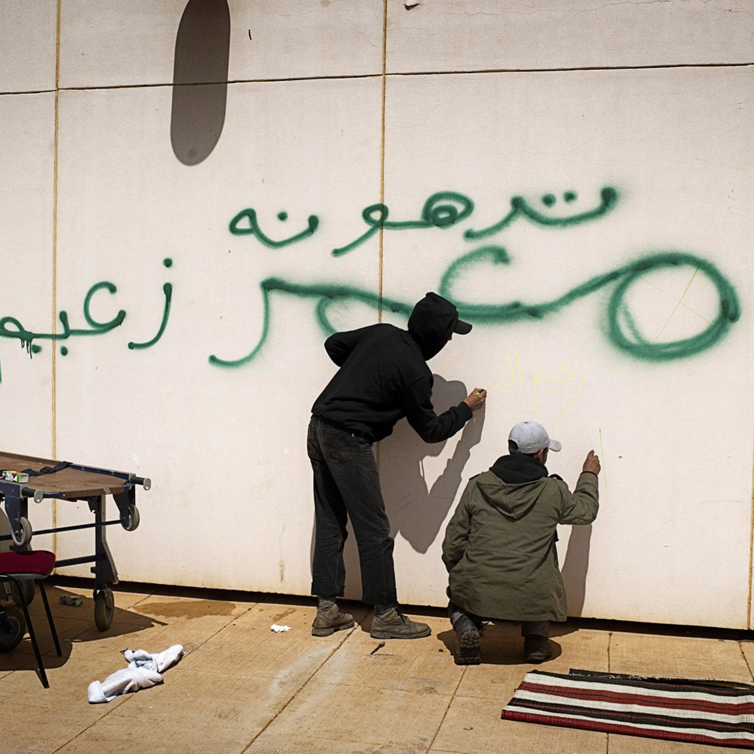 Libyan rebels scrawl graffiti on a wall near a hospital in Ras Lanuf, March 27, 2011. The wall was previously defaced, in green, by Gaddafi troops.