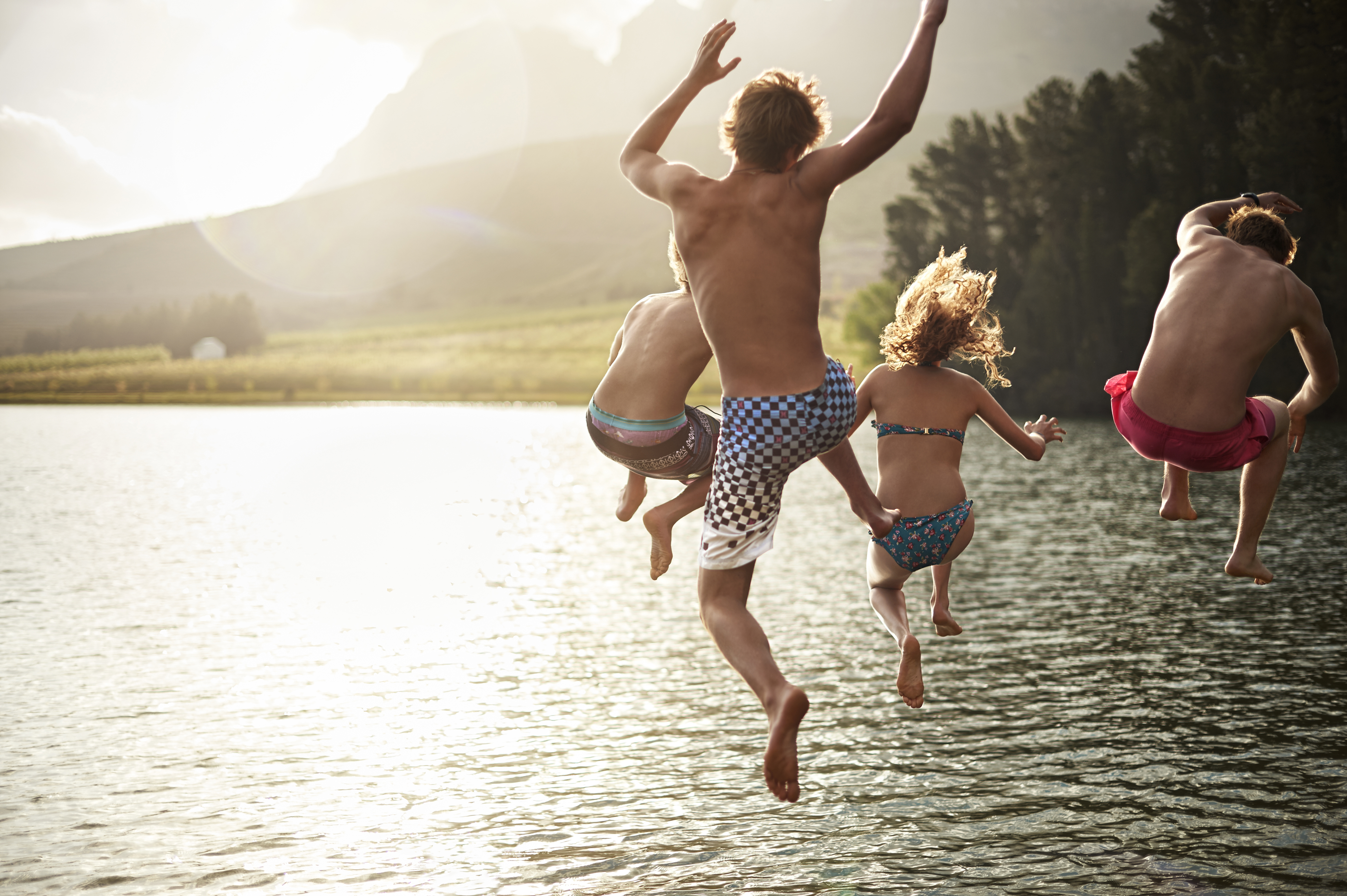 four friends jumping into a lake in the mountains