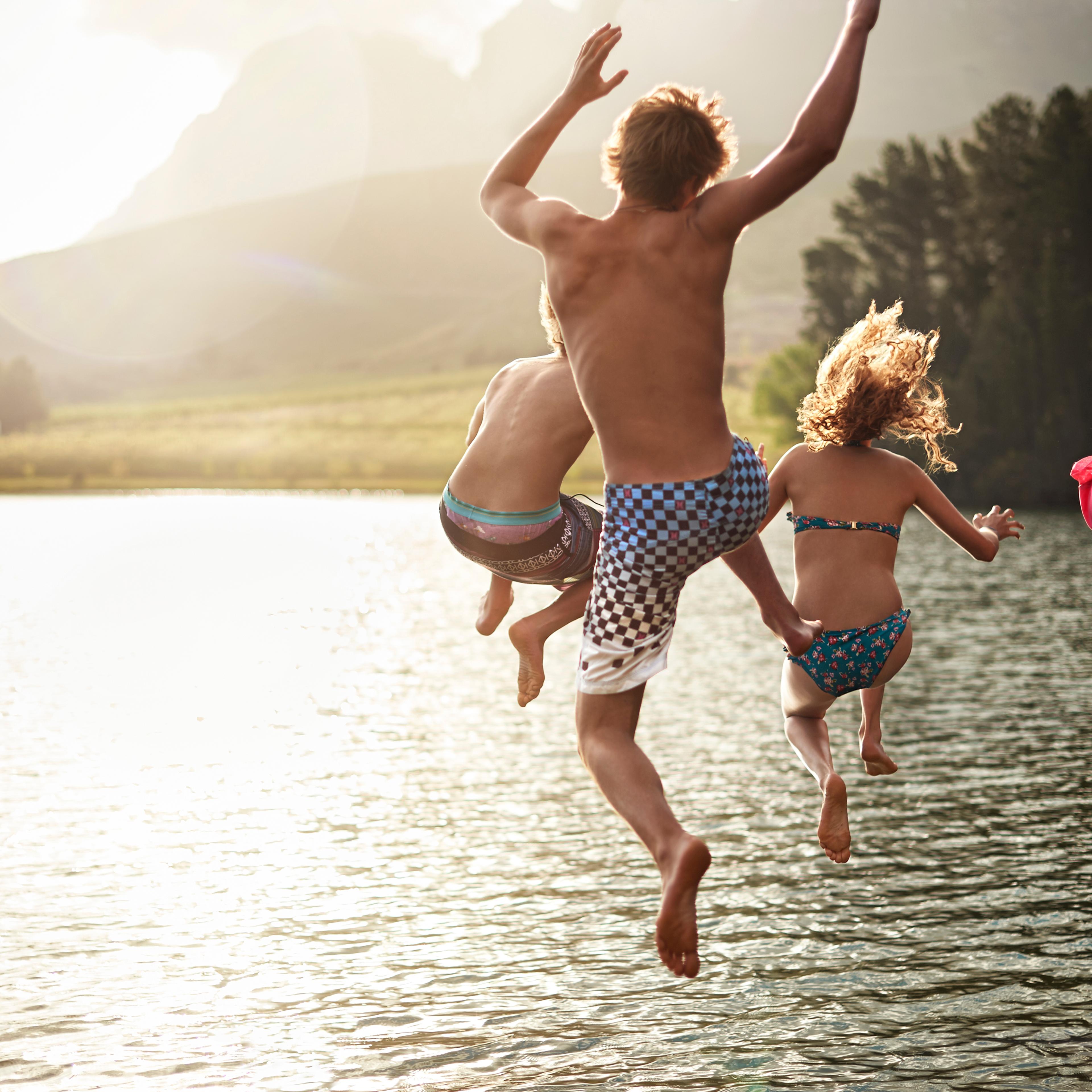 four friends jumping into a lake in the mountains