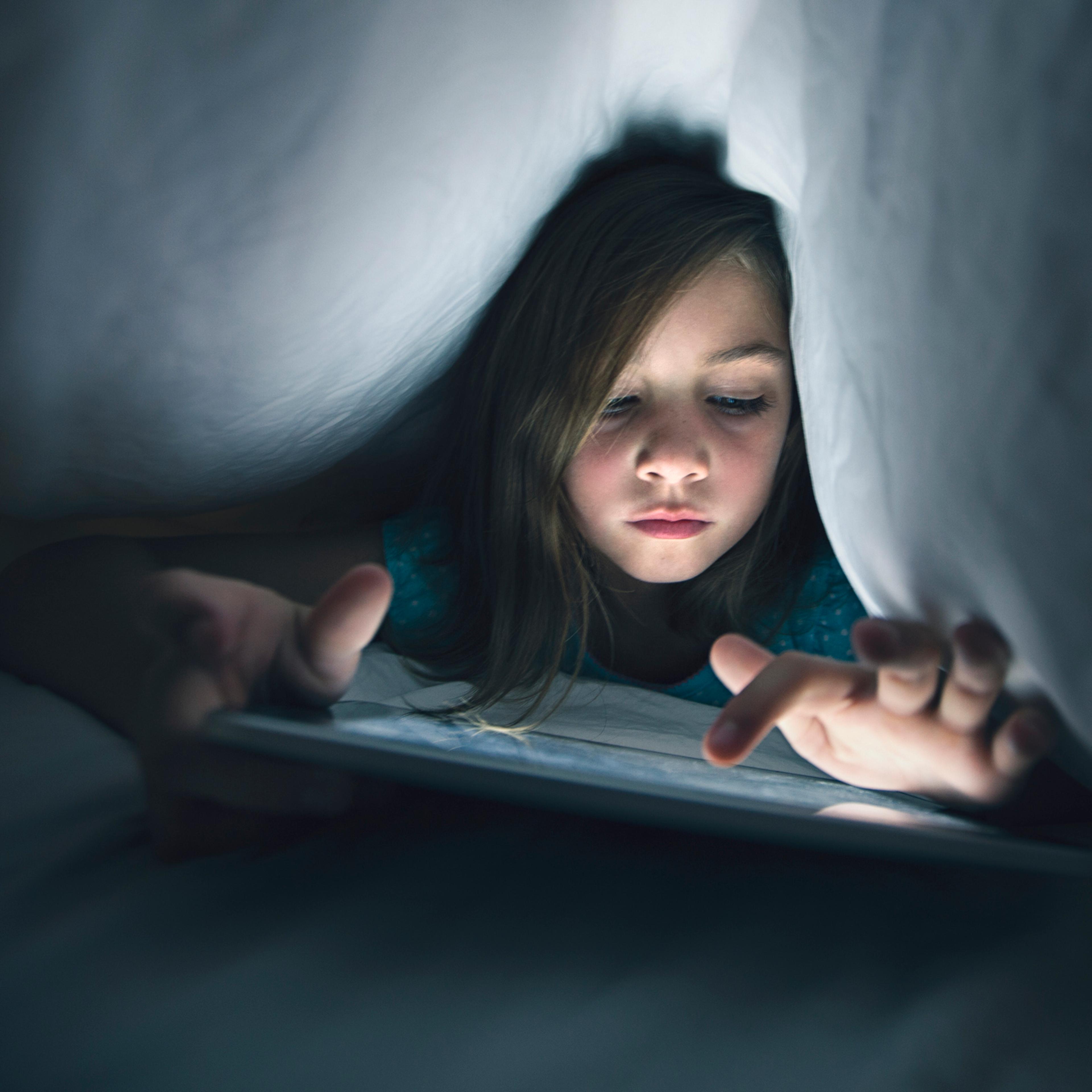 girl using wireless tablet under the bed covers