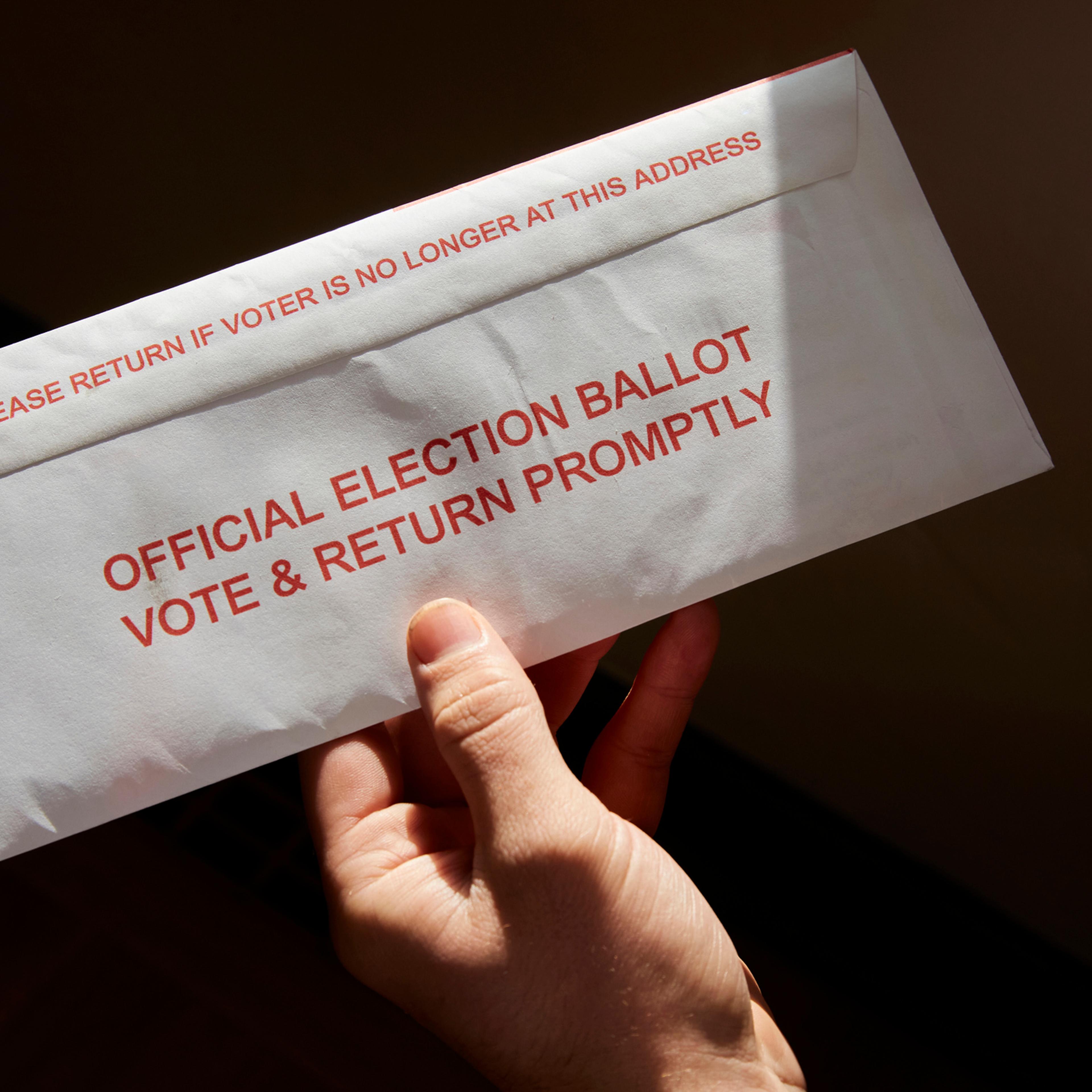 A person standing inside his home holding his mail in voting ballot