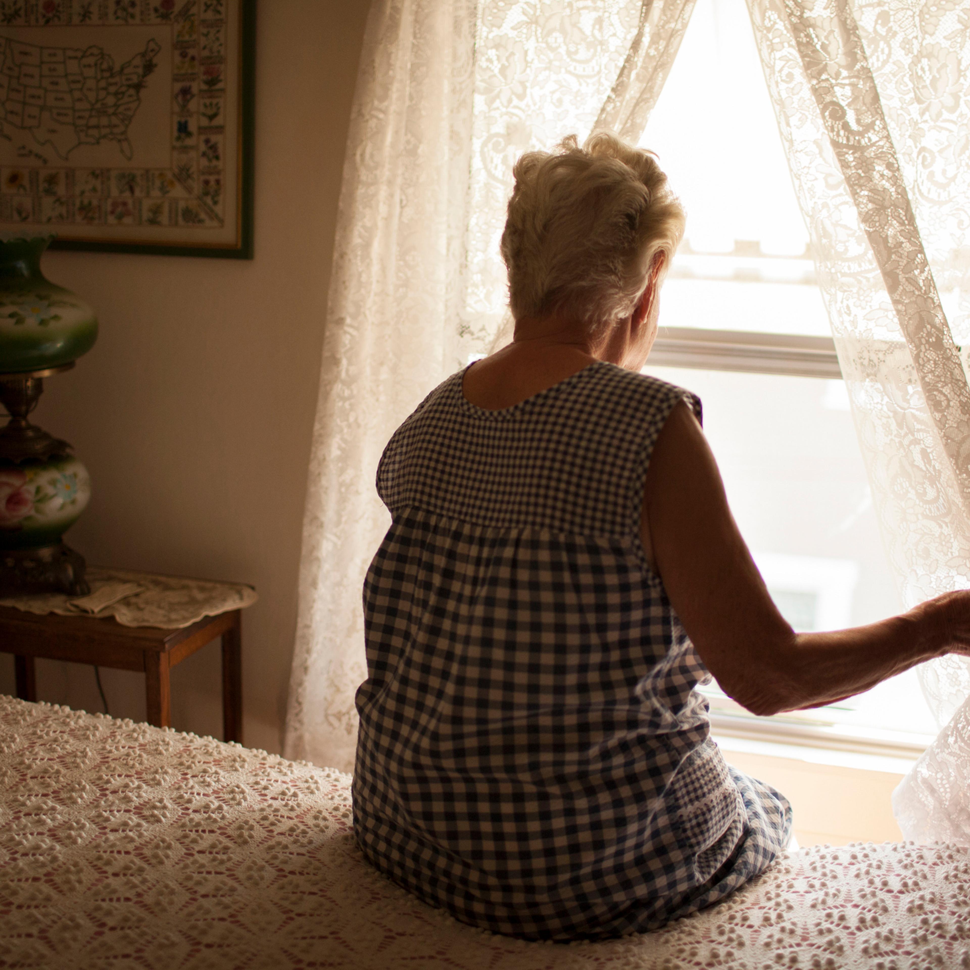 Pensive older woman looking out bedroom window